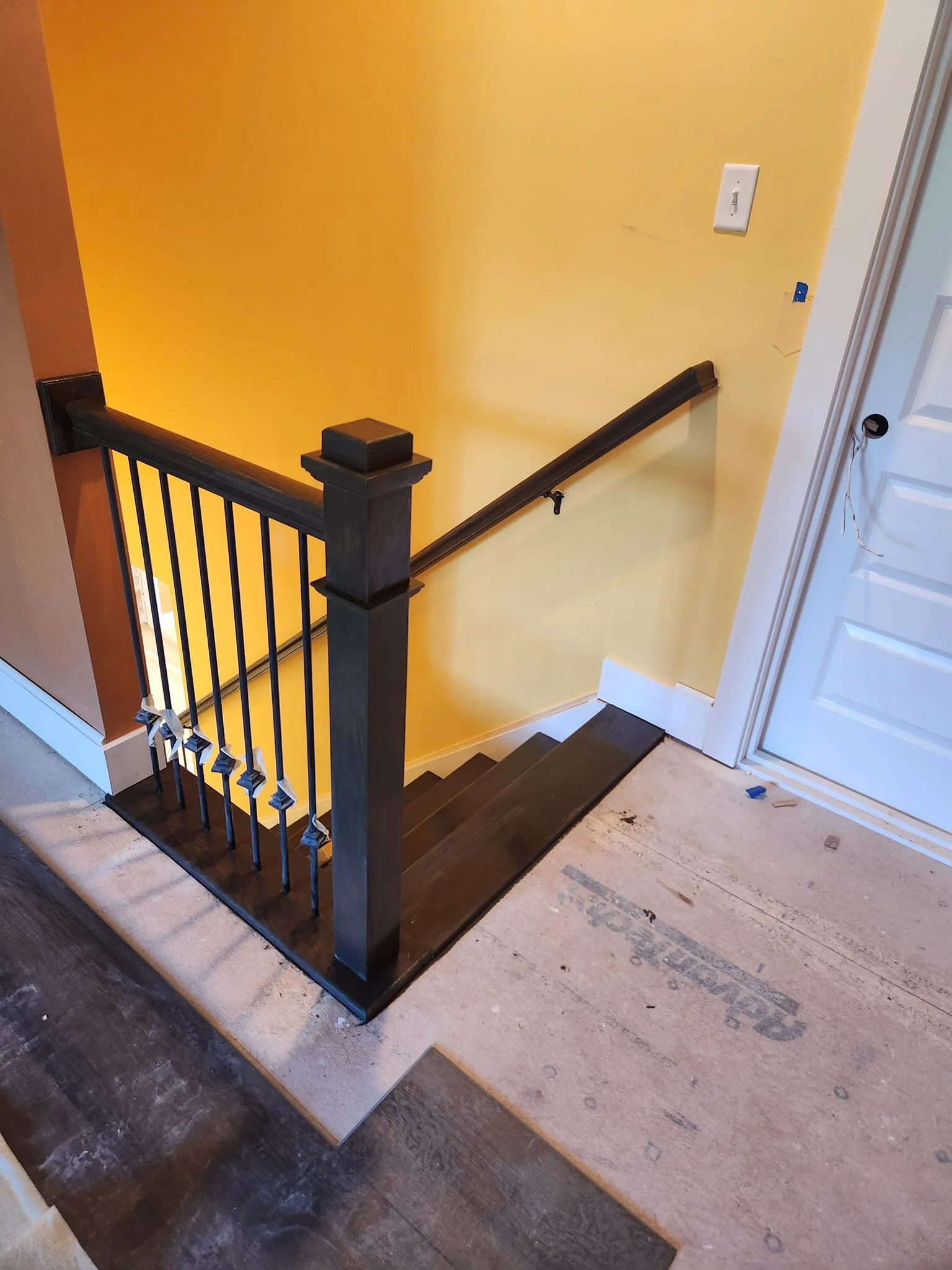 Interior view of a stairway with dark wood steps, black handrail, and a black balustrade with white wall and yellow wall in the background.