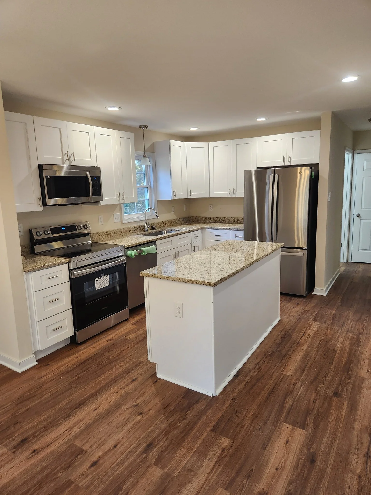 A modern kitchen with white cabinets, stainless steel appliances, a granite countertop island, and hardwood flooring.