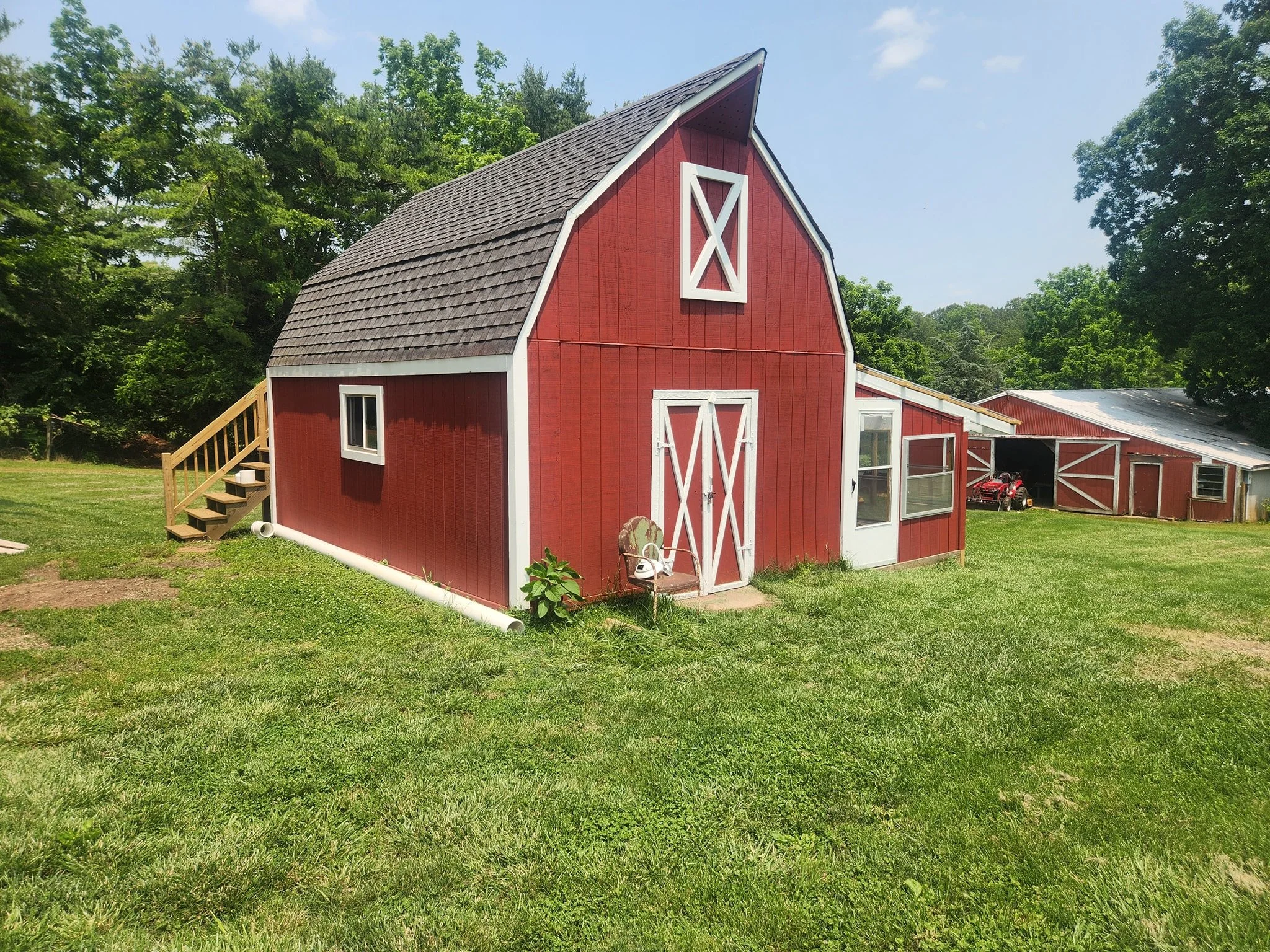 Red barn with white trim, small windows, and a staircase on the side, set in a grassy yard with trees in the background.