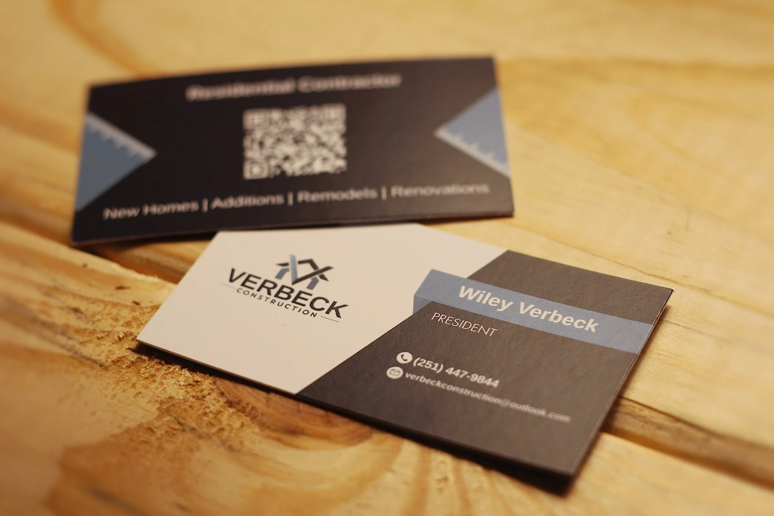 Business cards for Verbeck Construction and Wiley Verbeck on a wooden surface.