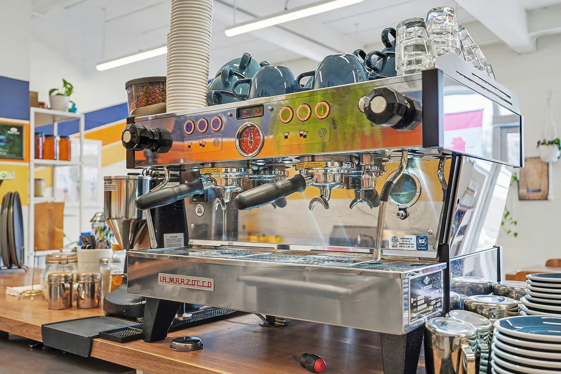 A professional espresso machine with cups and glasses on top, situated on a wooden counter in a cafe or restaurant setting.