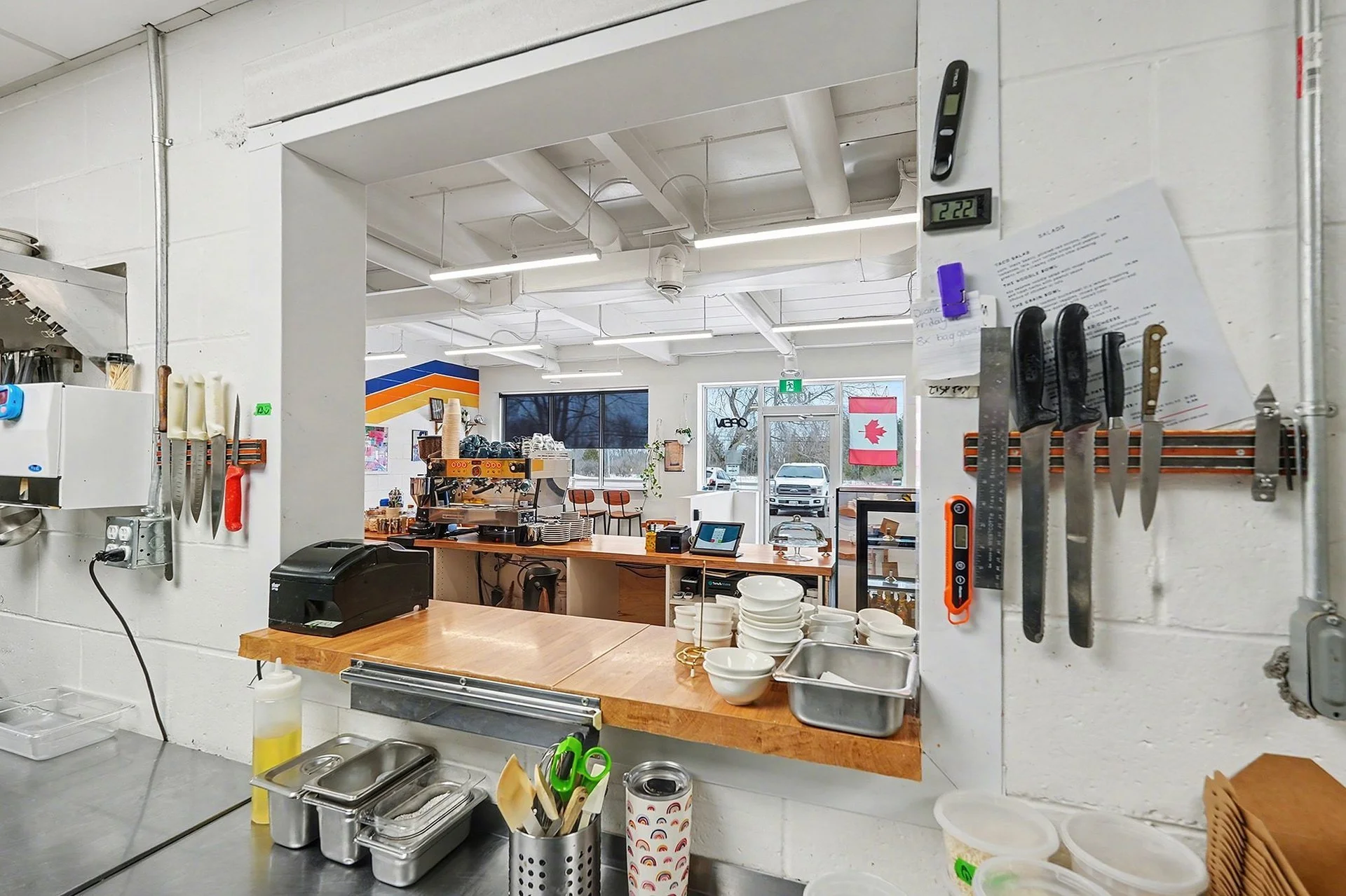 Interior view of a commercial kitchen with utensils on the walls, stacks of bowls, and a coffee machine on the counter in the background.