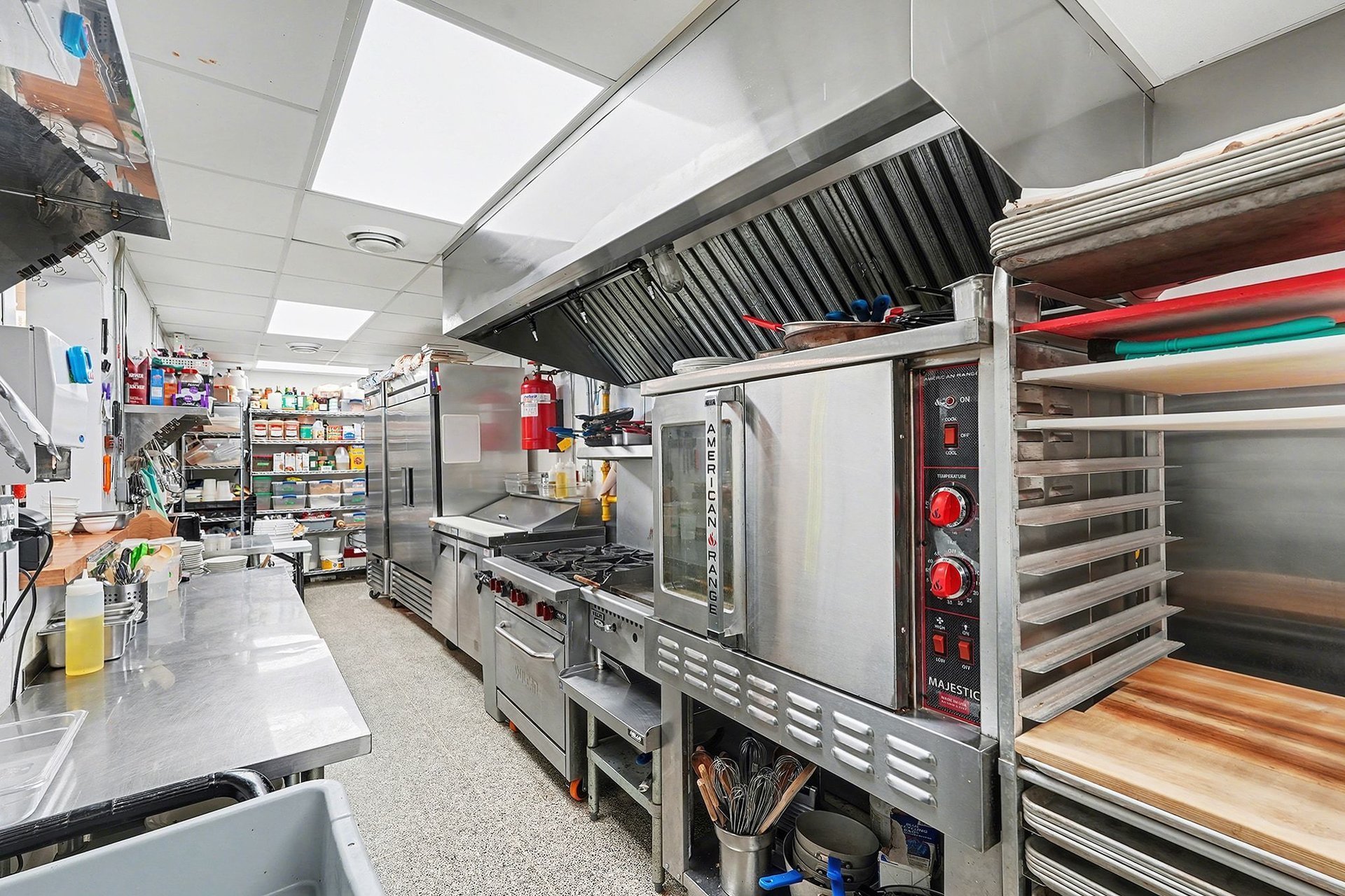 Commercial kitchen with stainless steel appliances, shelves with kitchen tools, and cooking equipment