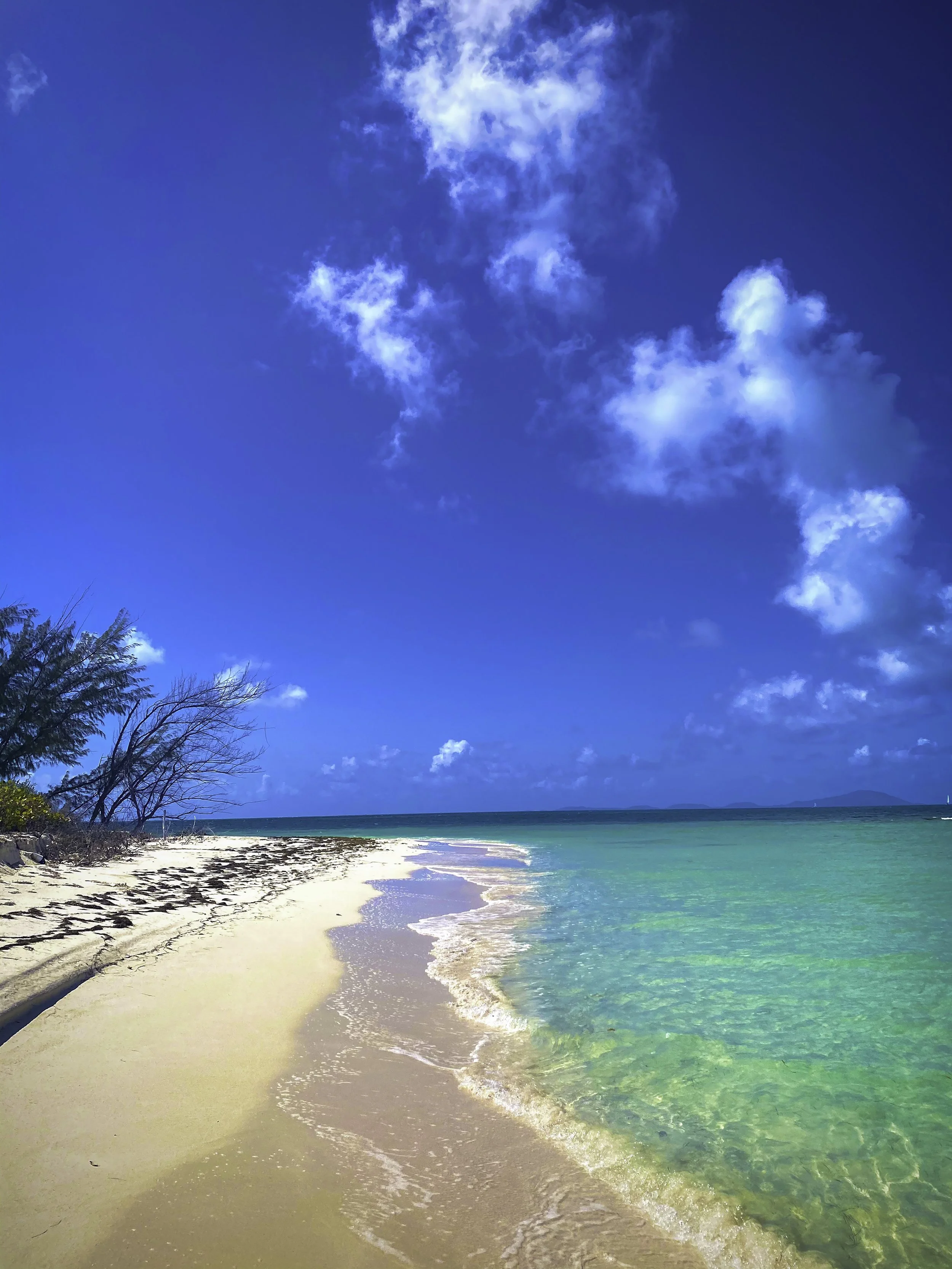 Tropical beach with white sandy shoreline, turquoise water, and a bright blue sky with scattered clouds.
