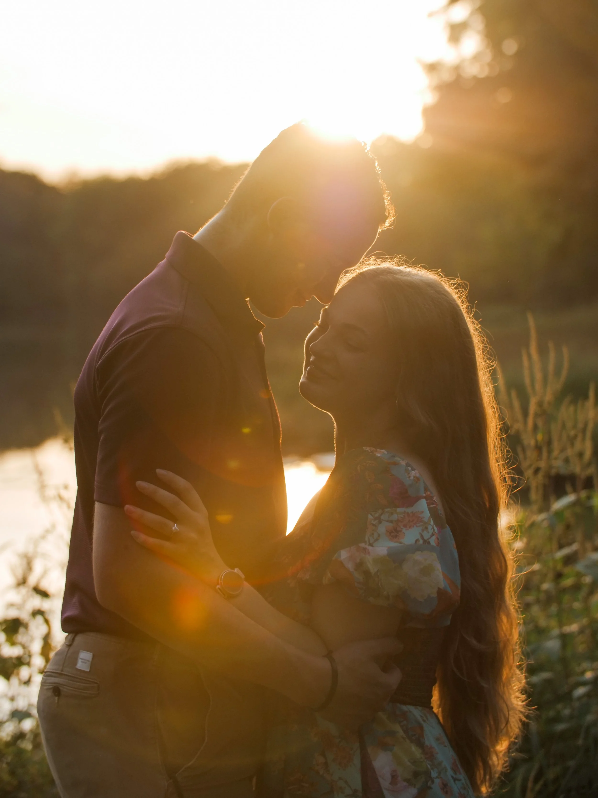 A couple standing close together outdoors during sunset with their foreheads touching, sharing an intimate moment.