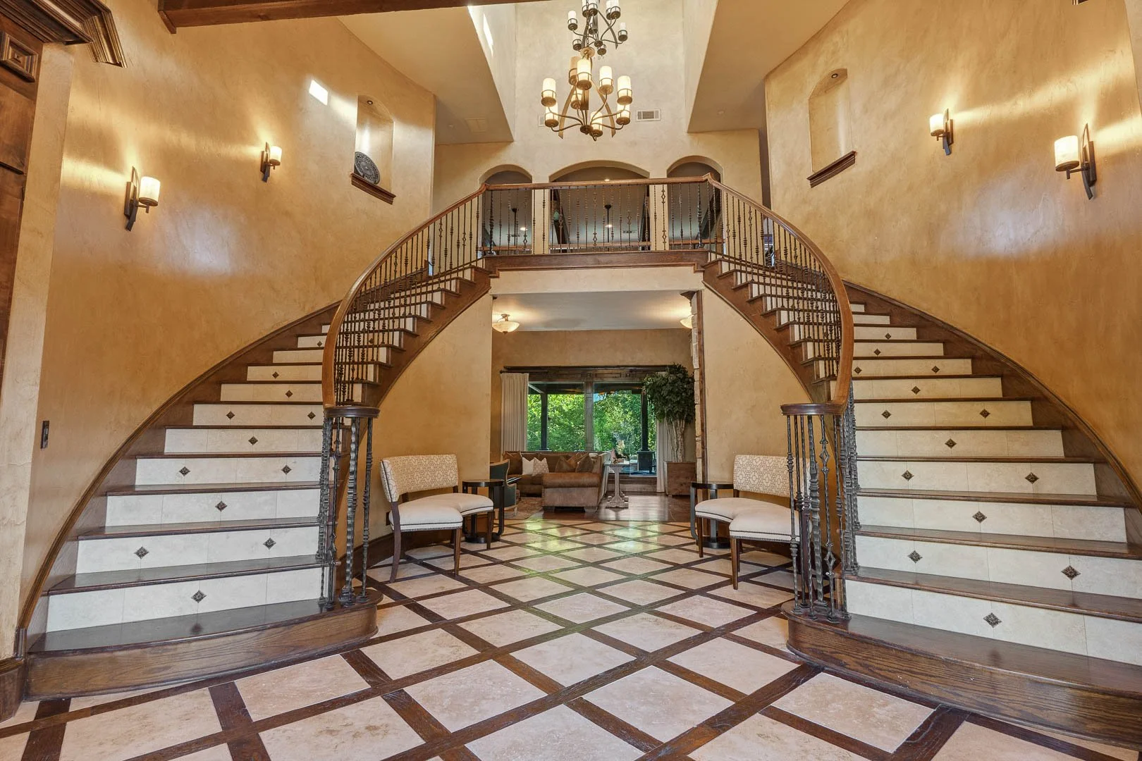 Elegant hotel lobby with a grand curved staircase, seating area, and large window showing greenery outside.