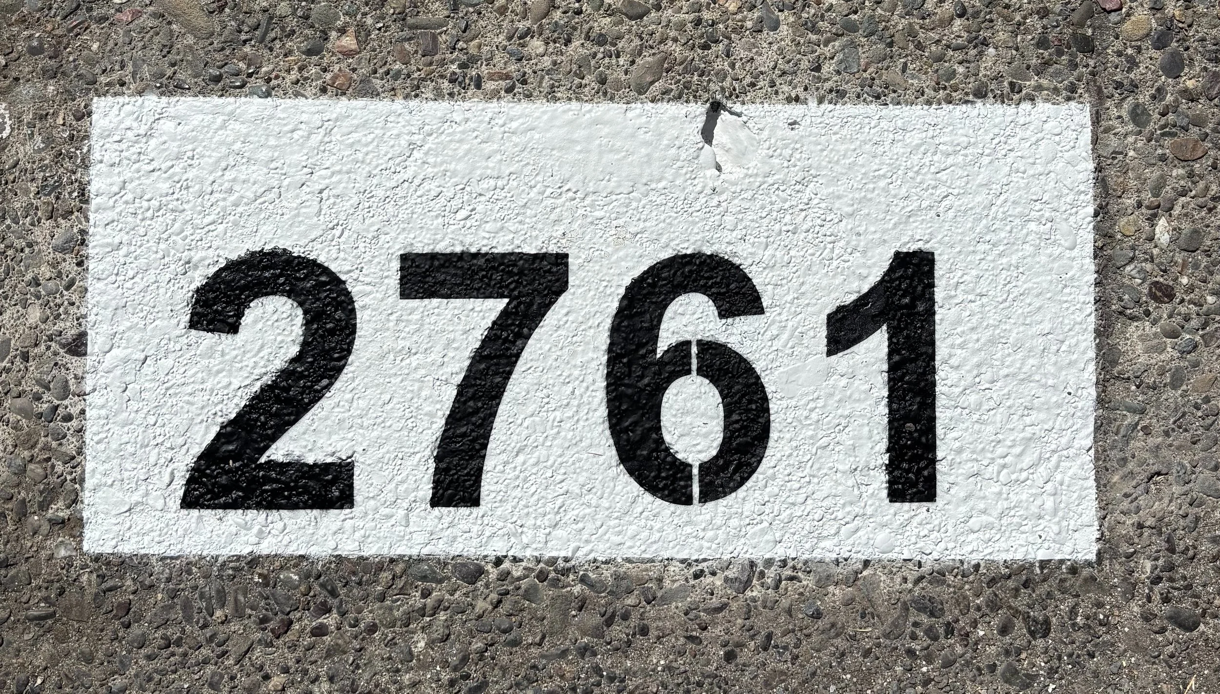 Newly painted curb address number embedded in asphalt with white painted background with the numbers 2761 in black.