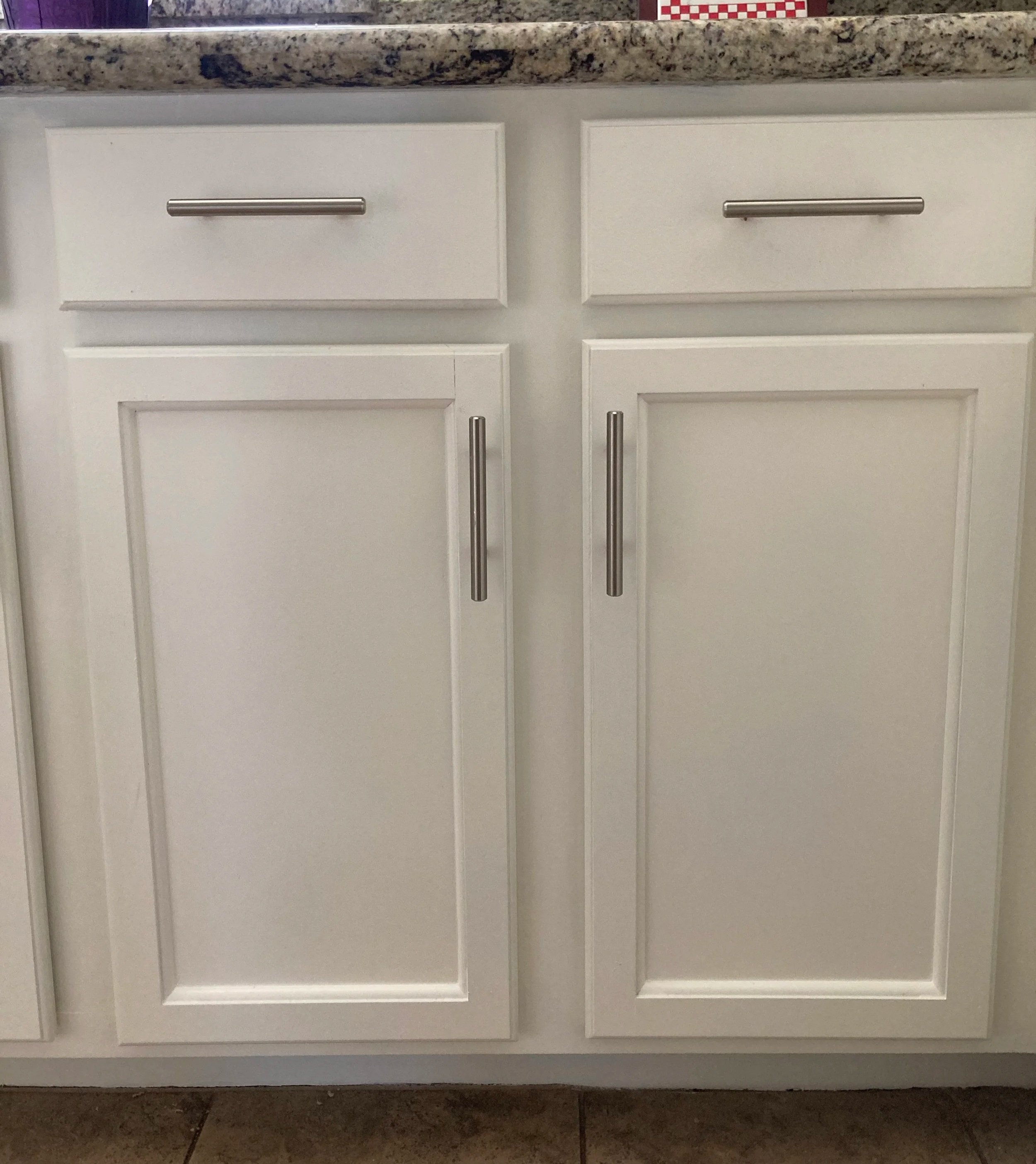 Newly painted white kitchen cabinet doors with silver handles, topped with a speckled granite countertop.
