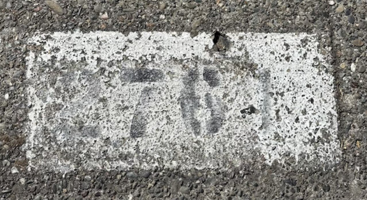Extremely old and deteriorated curb address number embedded in asphalt with painted black number 11 and white outlined border.