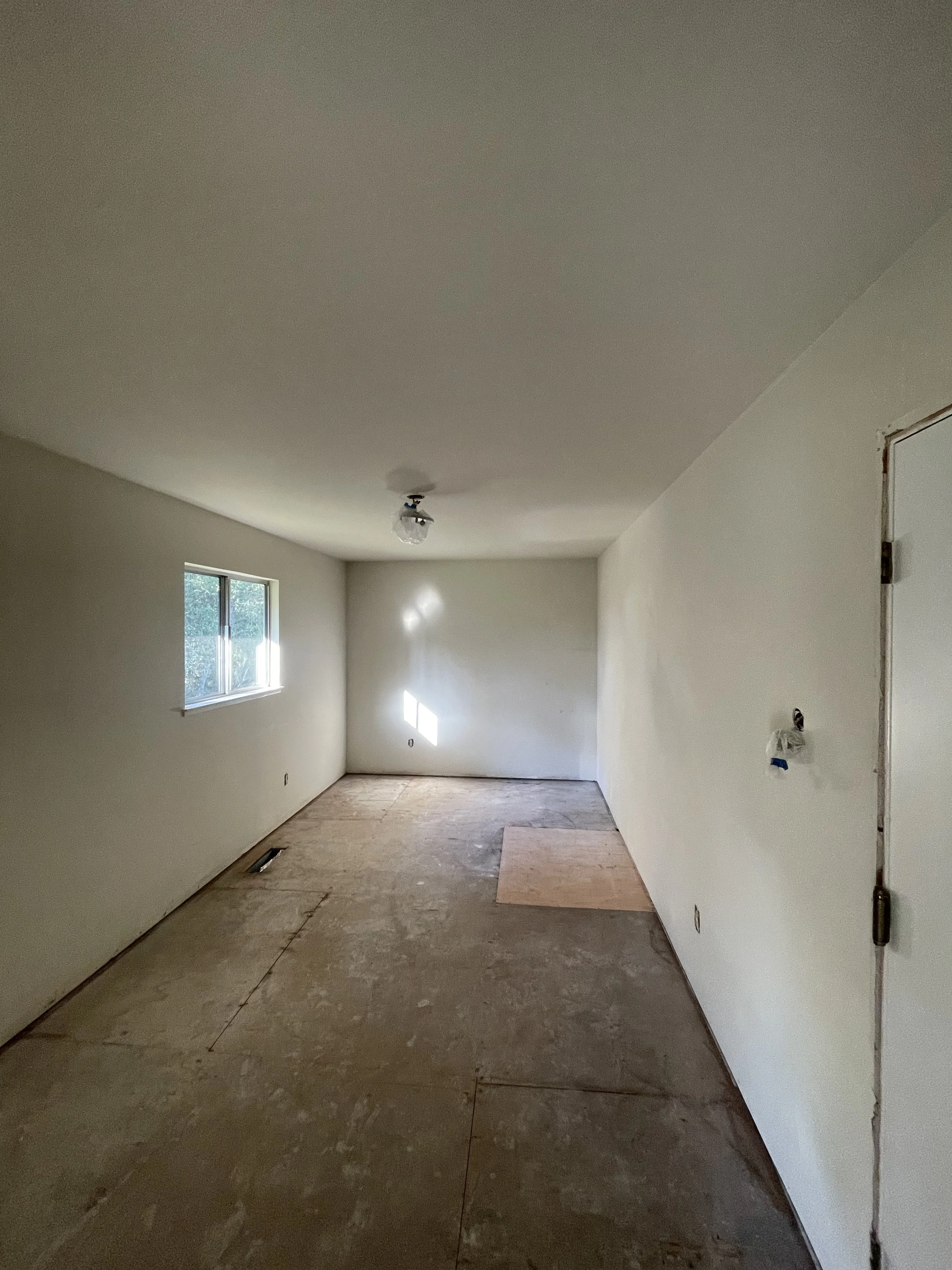 Empty room under construction with a window, a ceiling light fixture, and exposed electrical wiring.