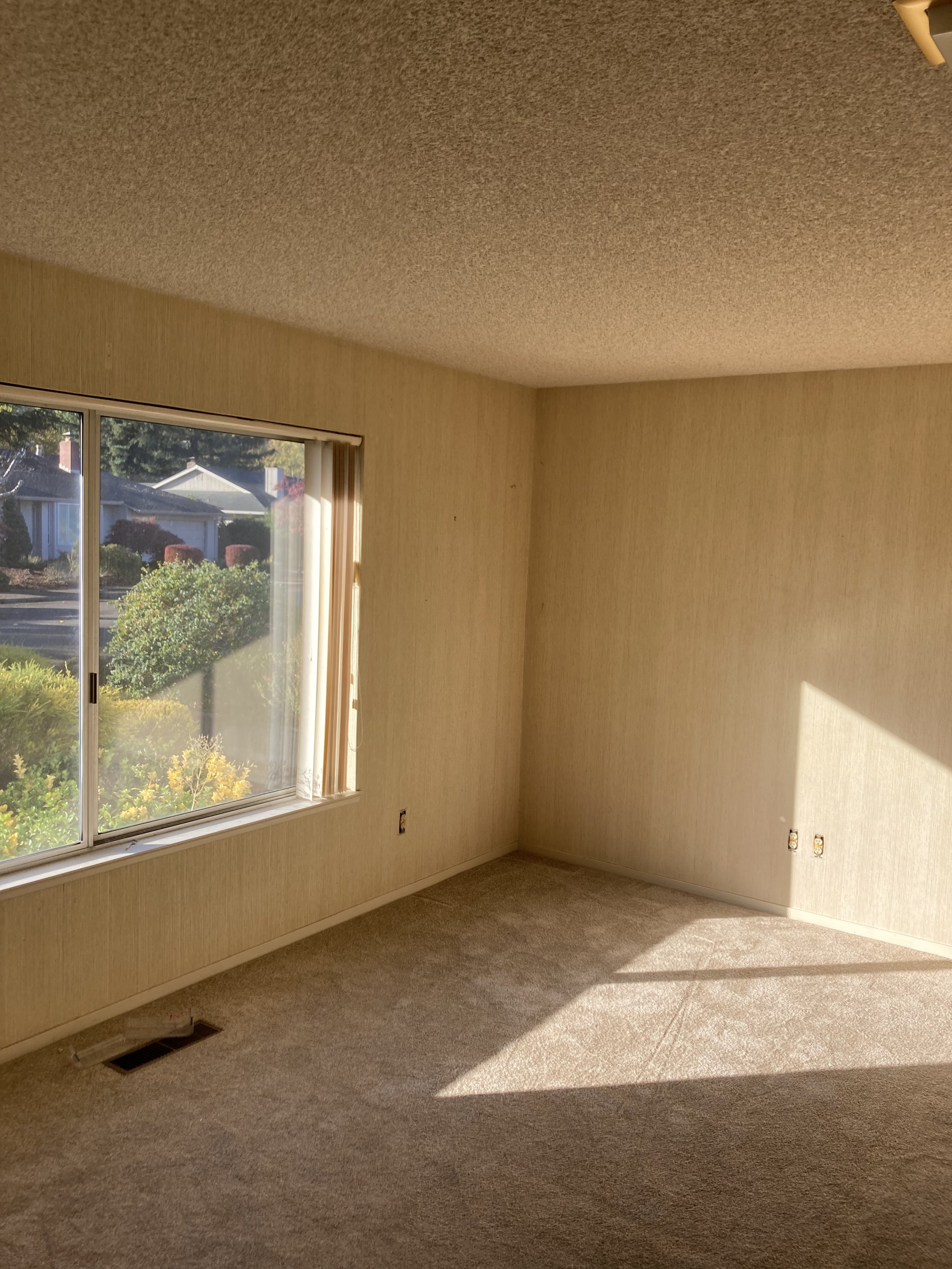 Empty room with beige carpet, dirty beige walls, a large window, and a ceiling vent.