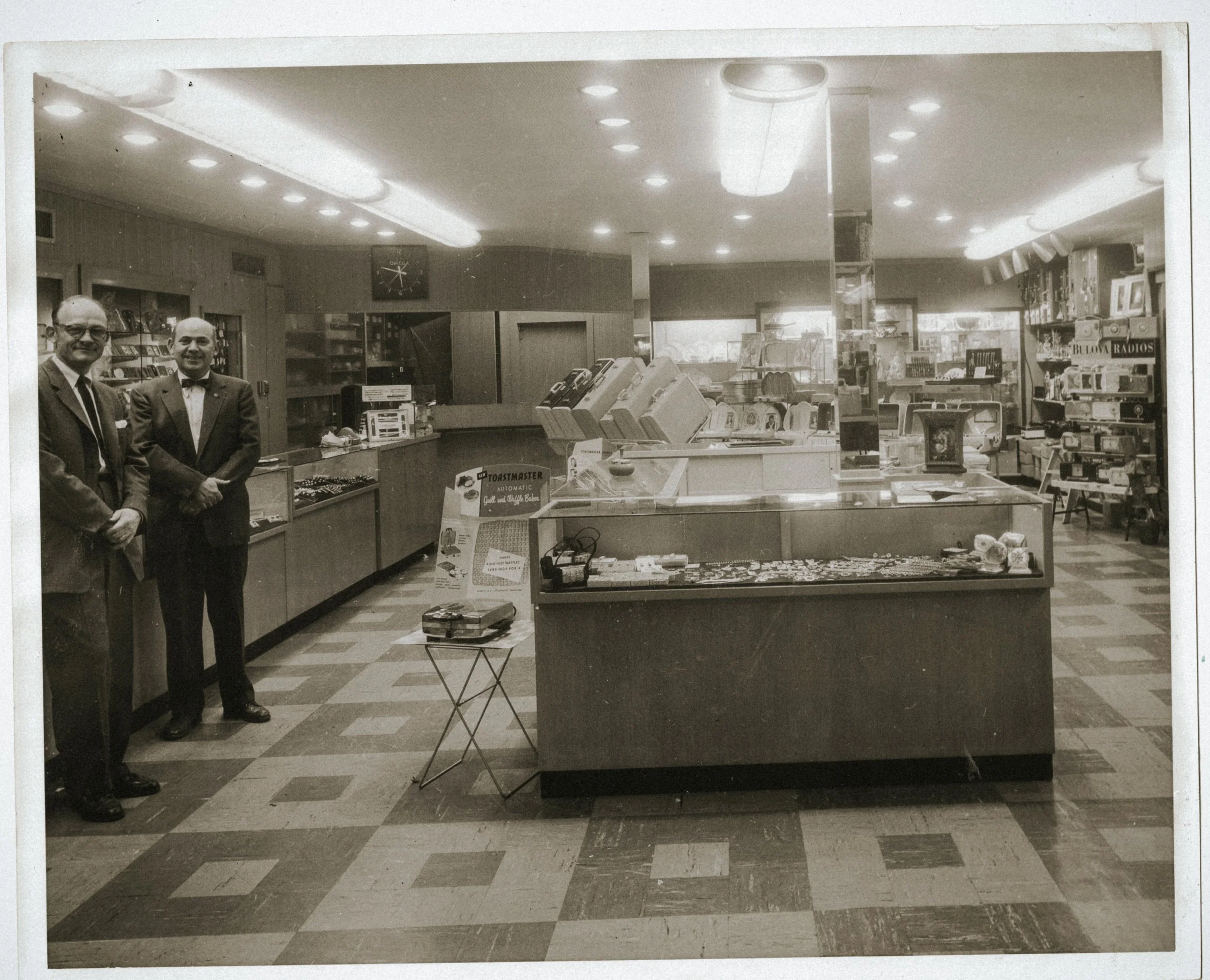 the original interior of simms with tile flooring, counters, and two men greeting