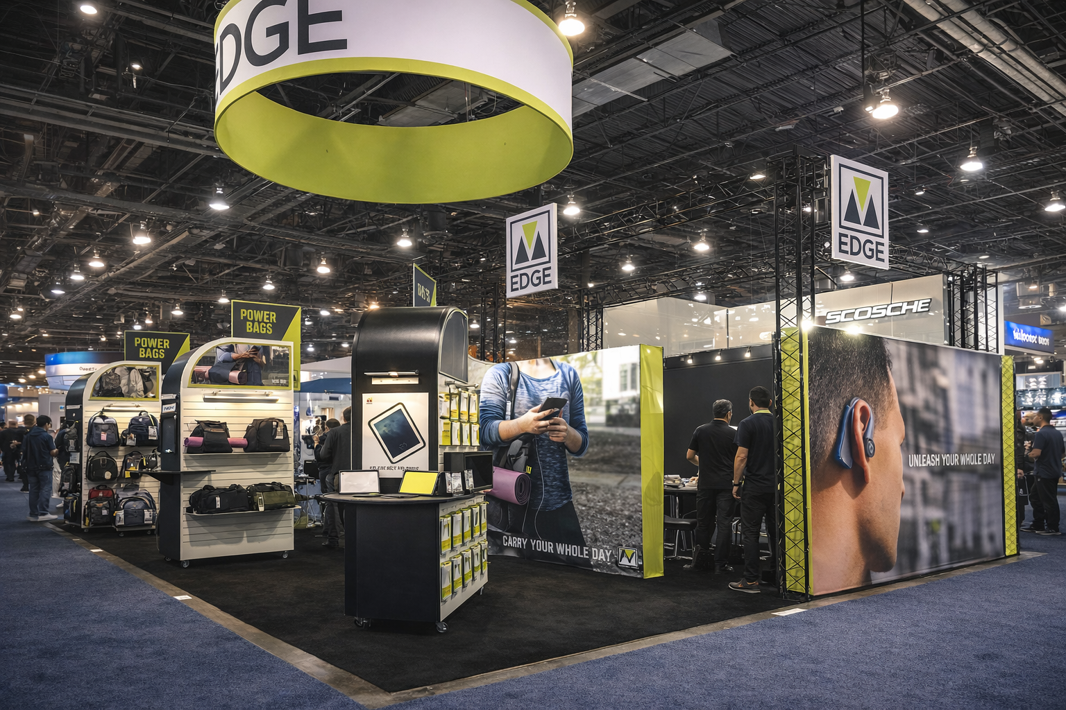 Trade show booth with backpacks, electronic accessories, and promotional banners for EDGE brand, featuring large poster of a man with wireless earbuds and a woman using a tablet, inside a busy exhibition hall.