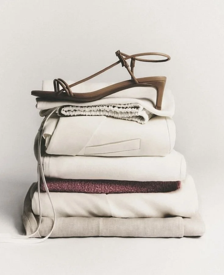 A pile of folded bedsheets and blankets with a tan sandal placed on top against a plain white background.