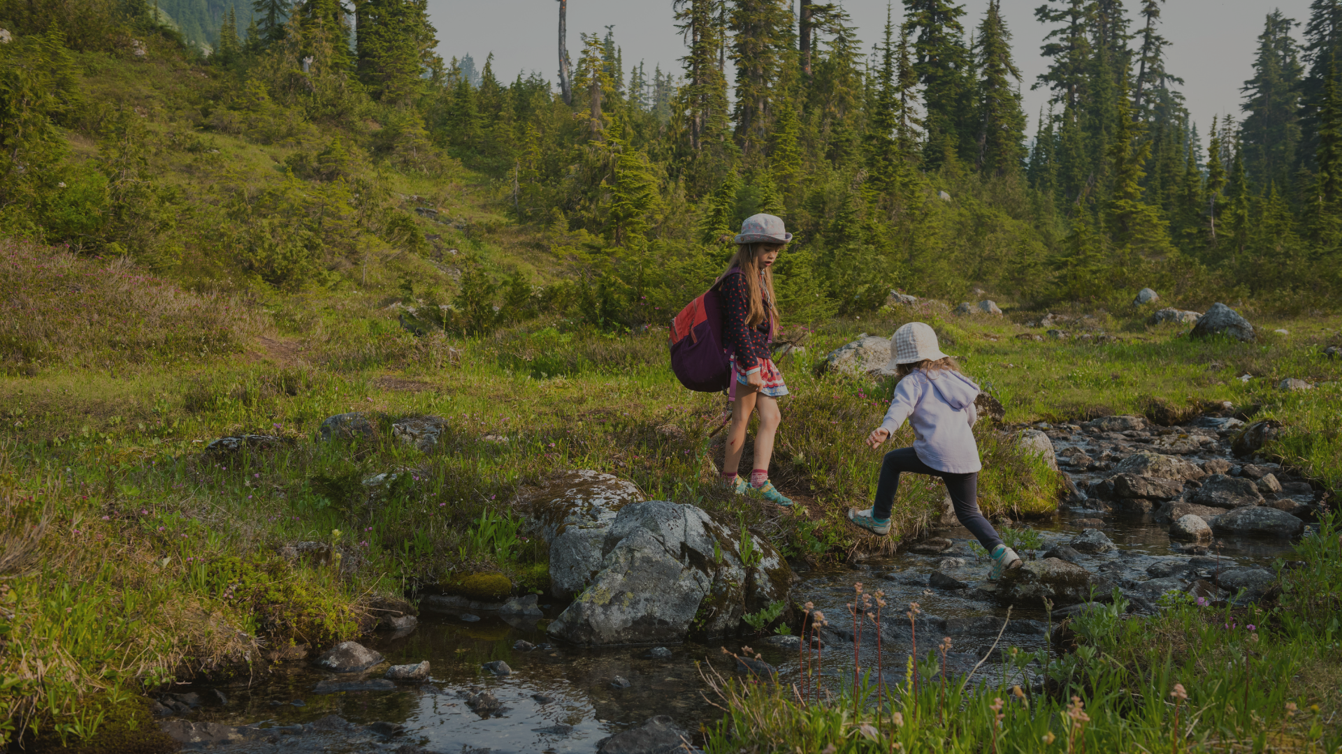 Big kid watching a little kid jump over a stream in the woods