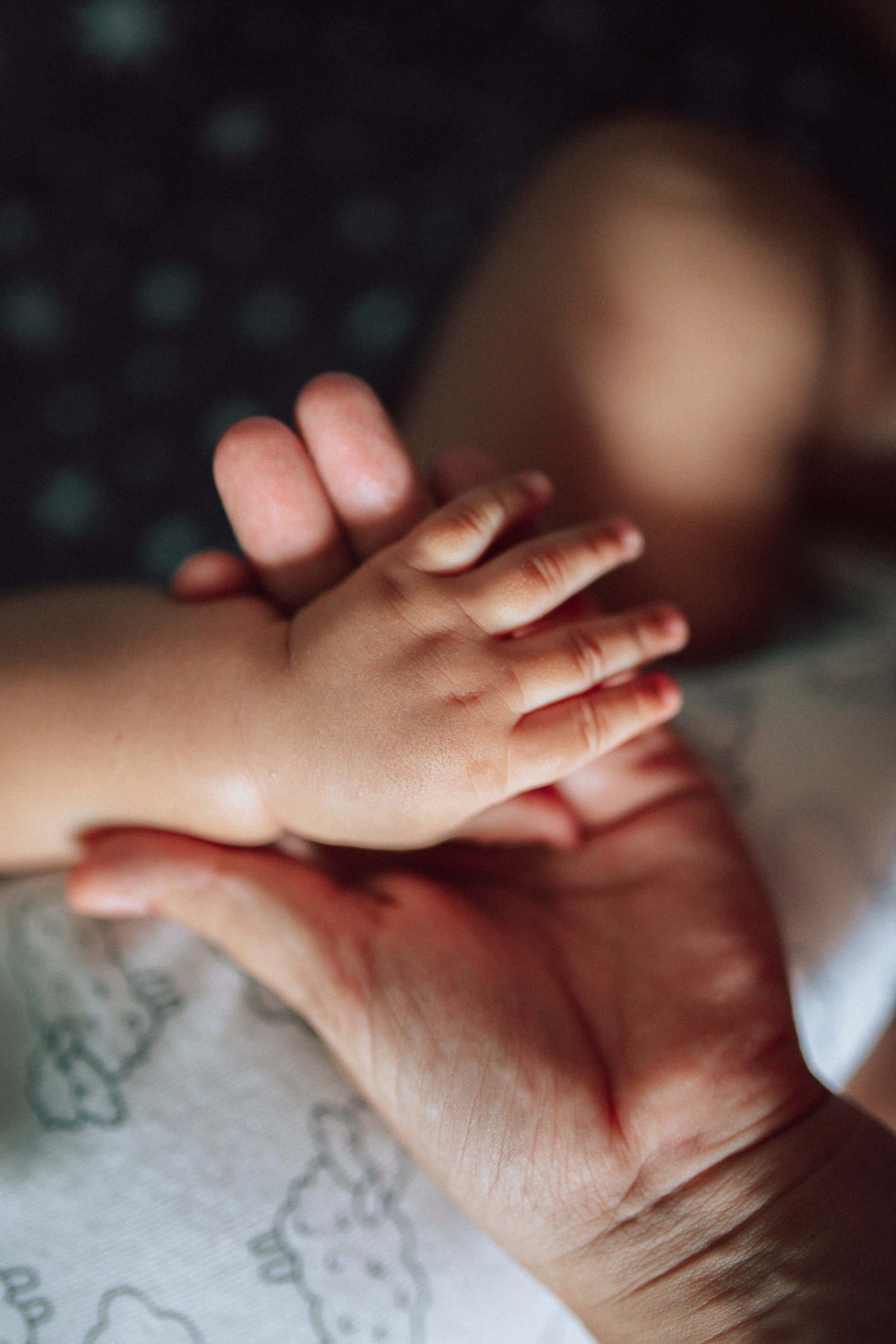 Close-up of a small child's hand gently resting on an adult's hand against a blurred dark background.