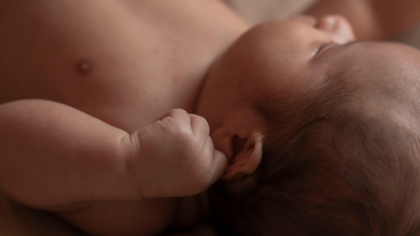 Close-up of a sleeping newborn baby with a clenched fist resting near its face.
