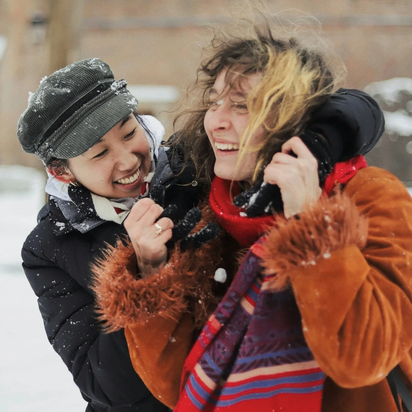 Two adult women laughing and playing in the snow.