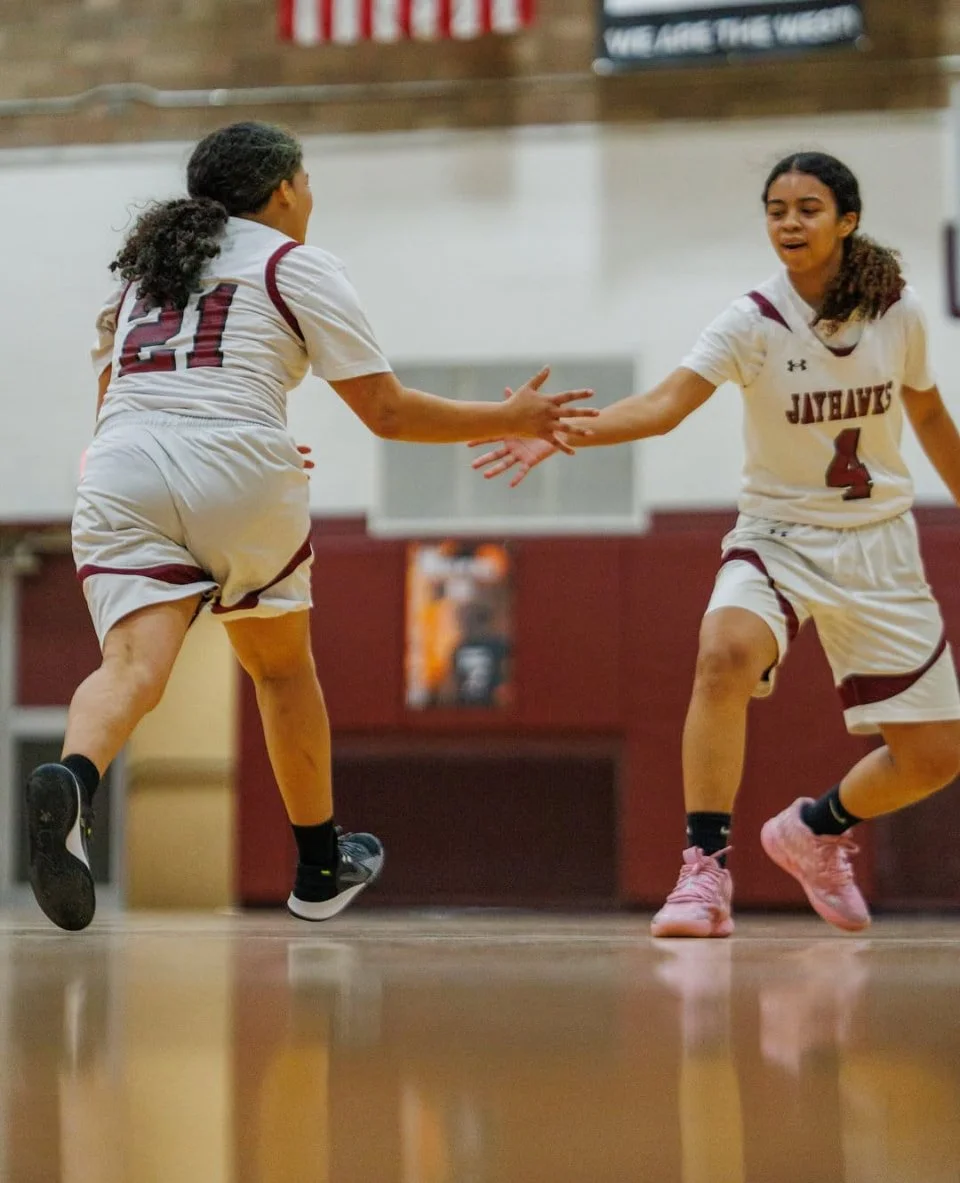 Two female basketball players in uniform high-fiving during a game.