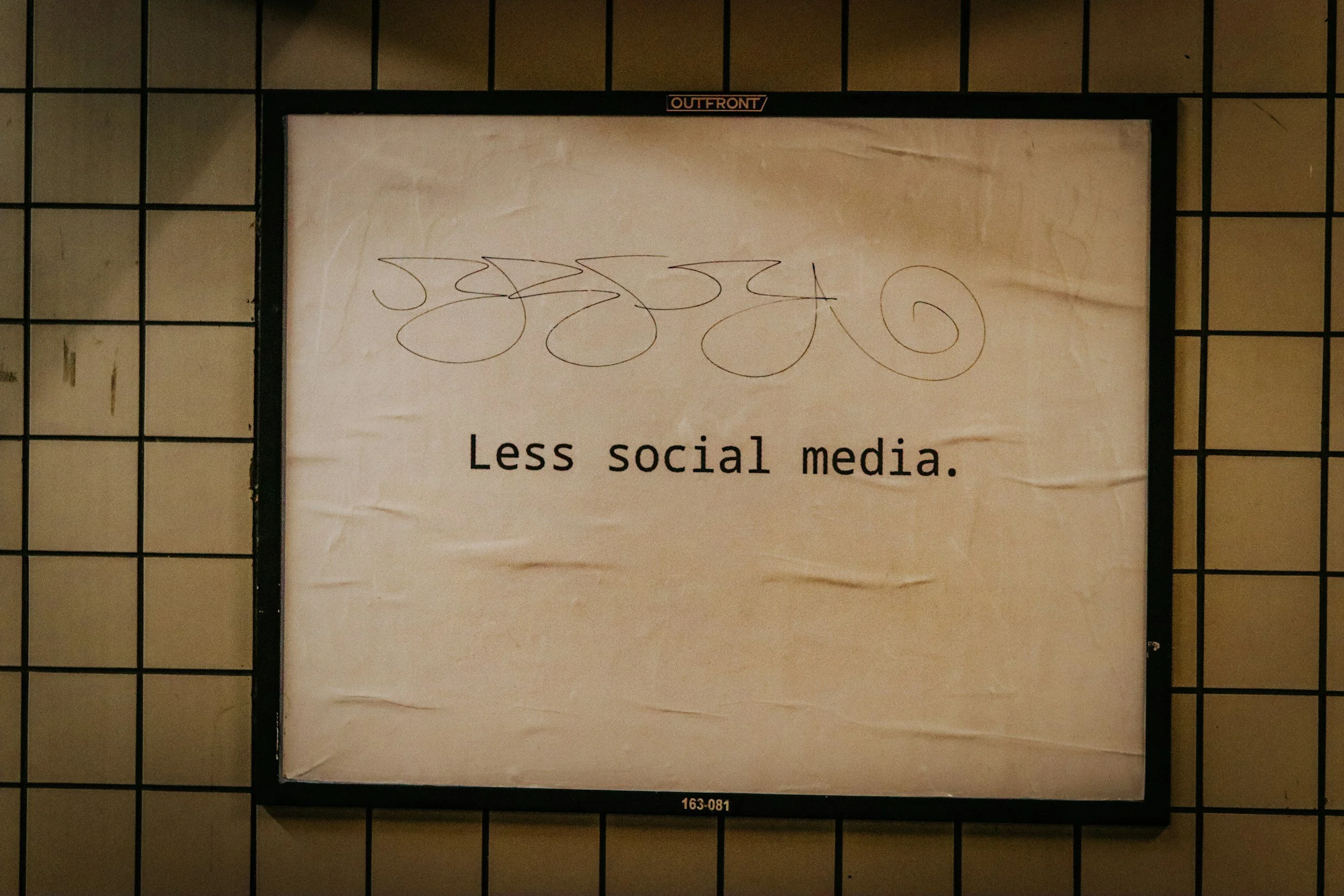 Digital sign with scribbles and the message 'Less social media.' on a tiled wall.