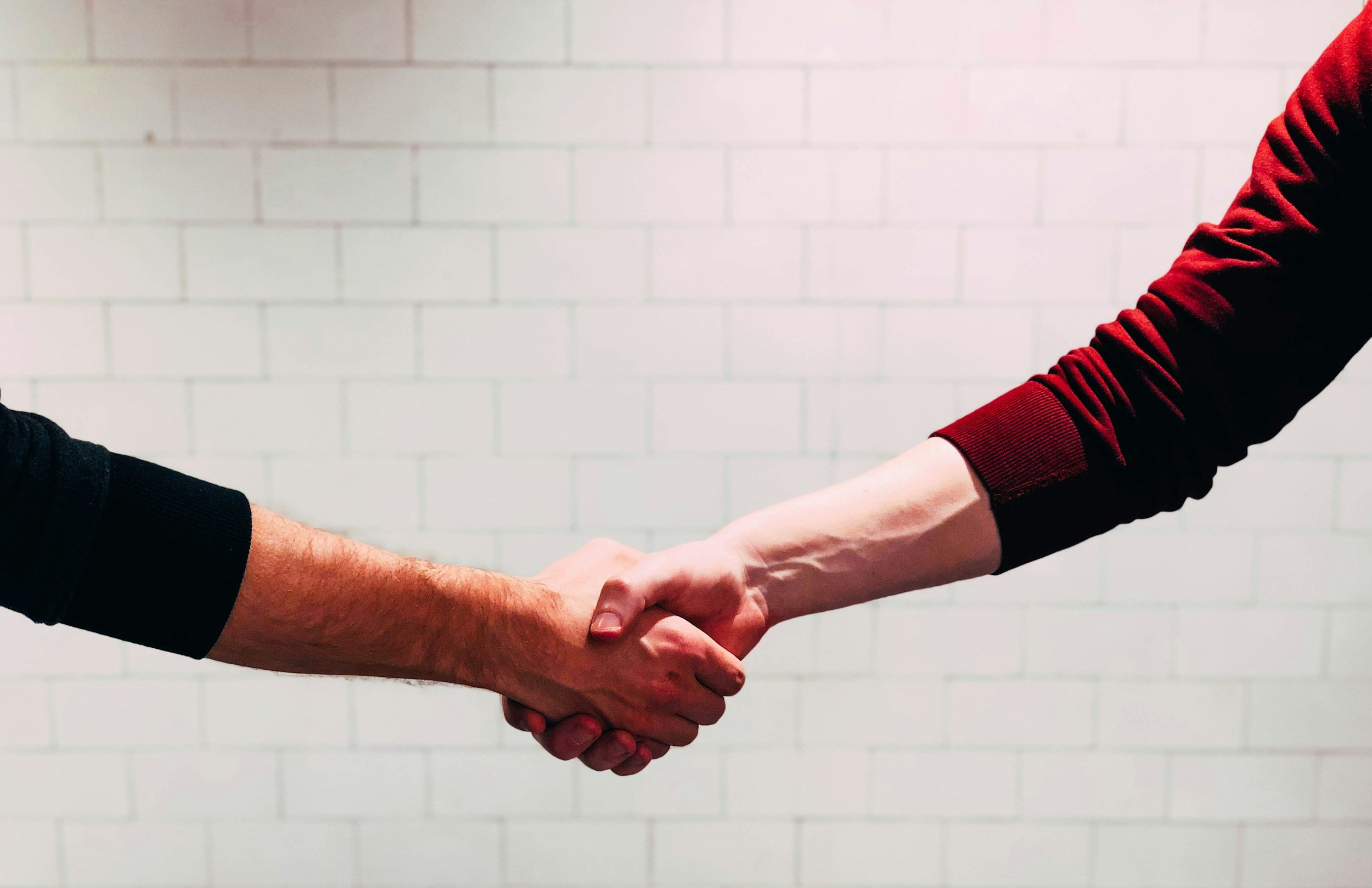 Two people shake hands against a white brick wall background.