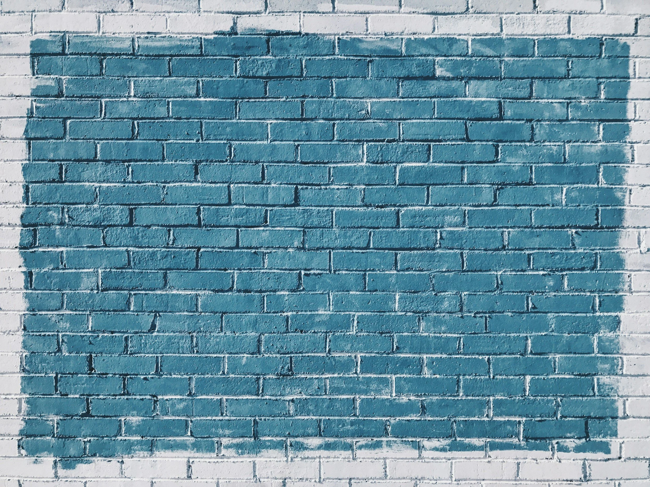 A painted brick wall with a large teal rectangle painted over a brick wall.
