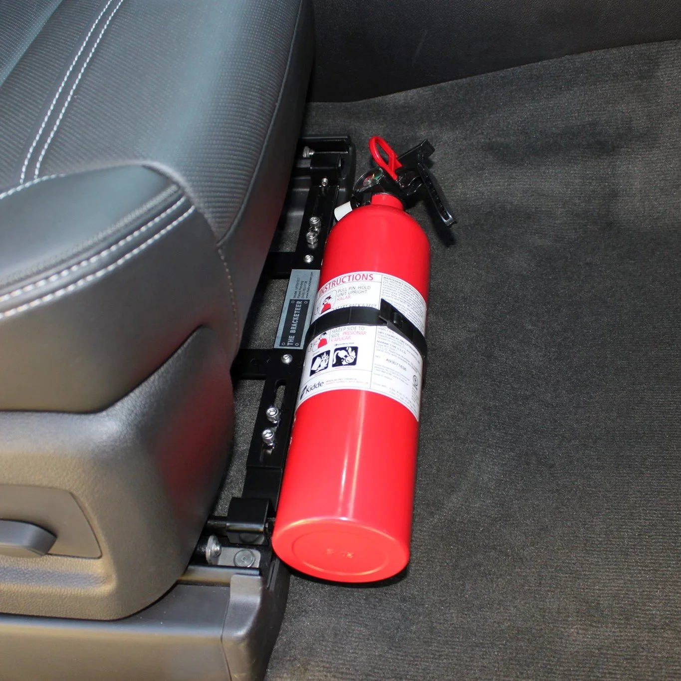 The Bracketeer fire extinguisher secured on the floor behind the front passenger seat in a vehicle.