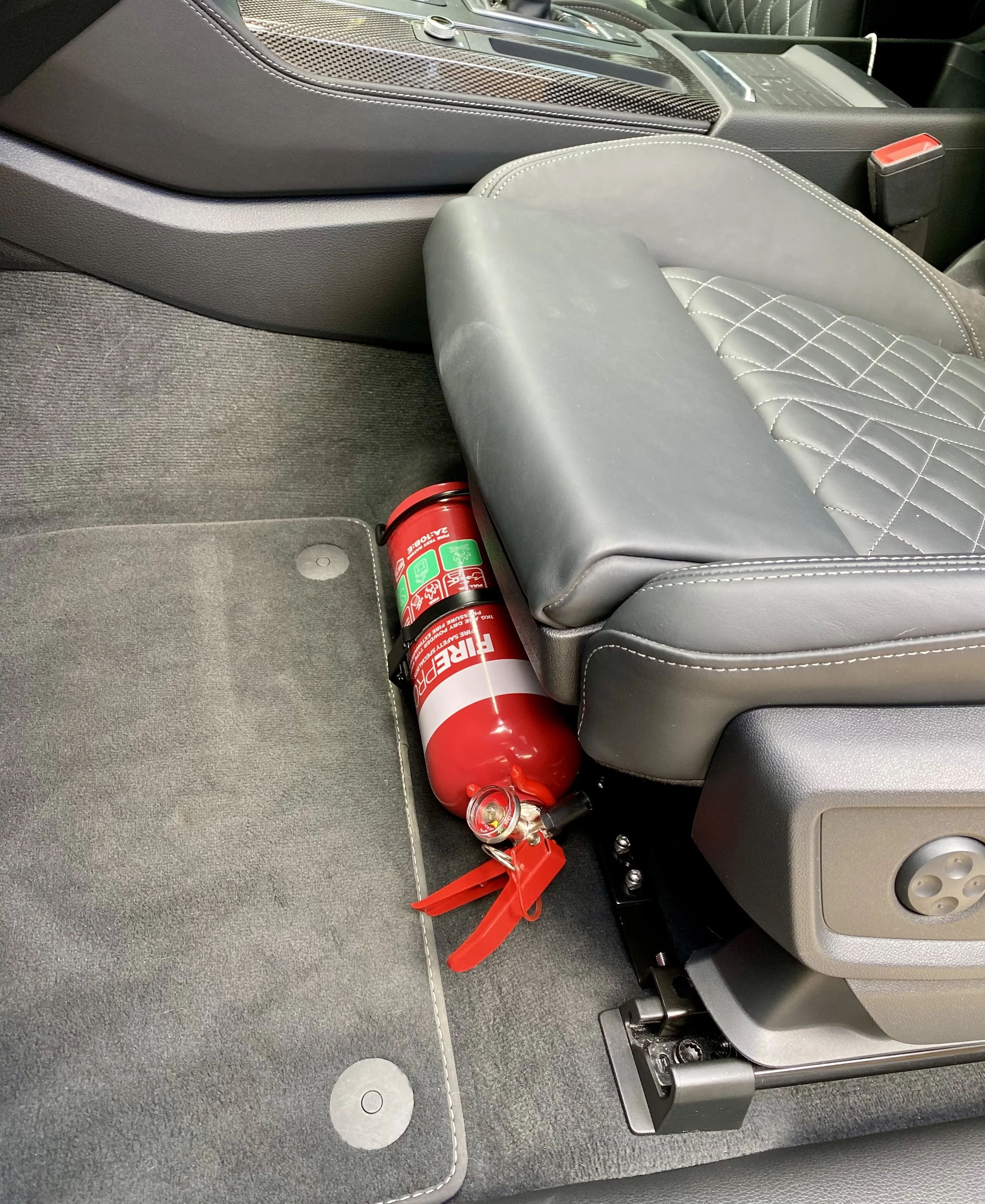 The Bracketeer Universal Fire extinguisher stored under a car seat in a vehicle interior.