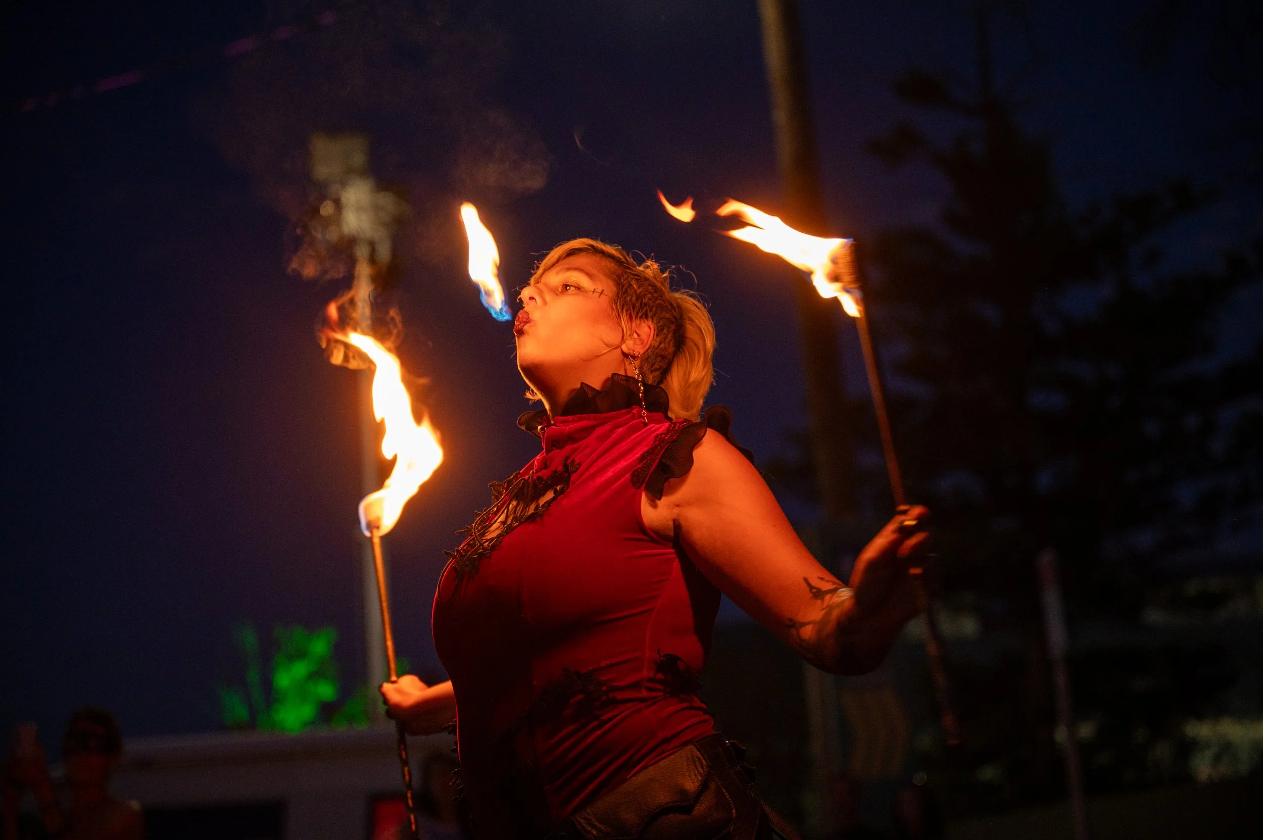 Person performing fire juggling at night, holding lit torches with flames illuminated in dark background.