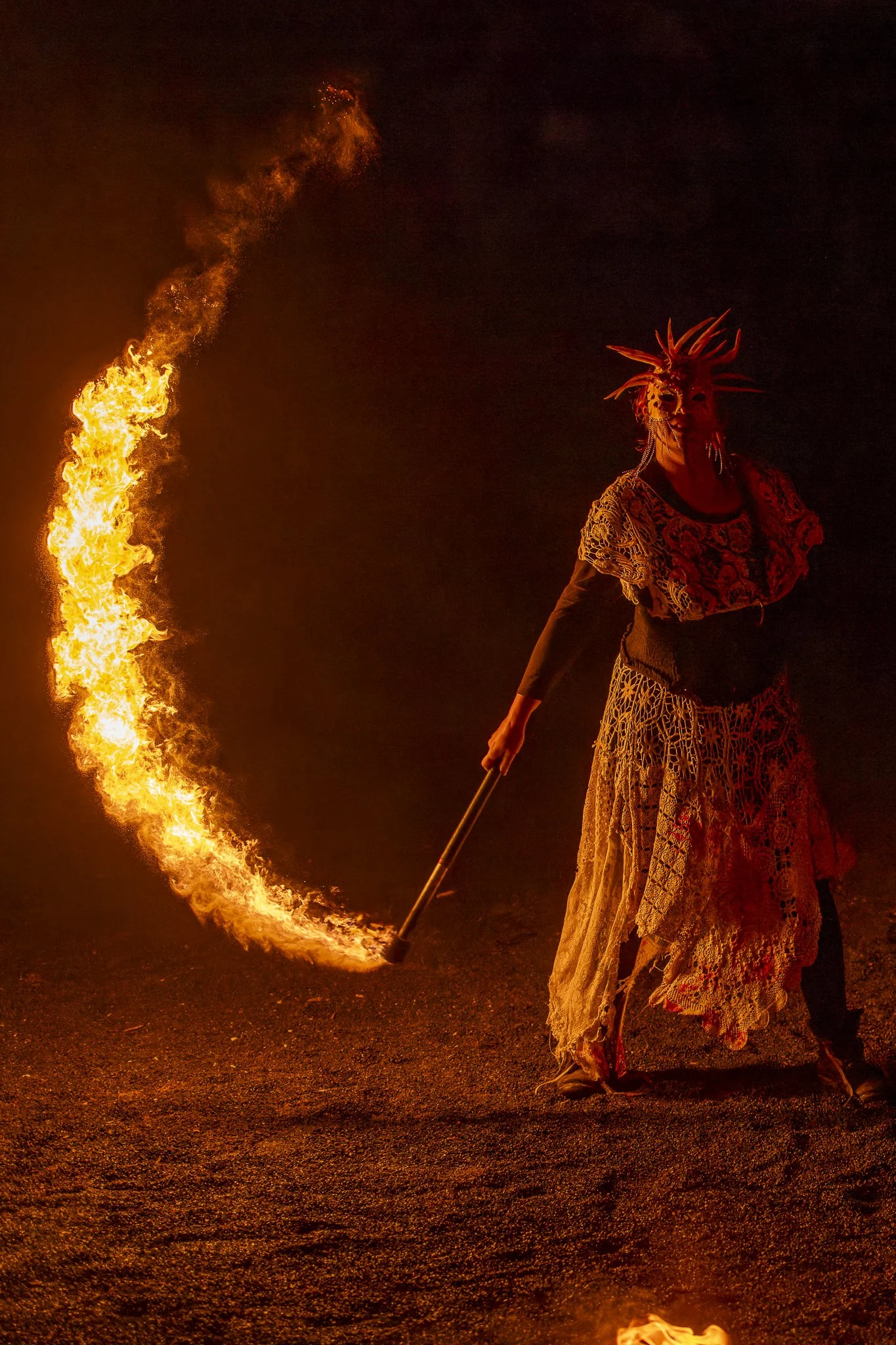 Performer in a costume with a spiked headdress holding a fire torch during a nighttime fire performance.