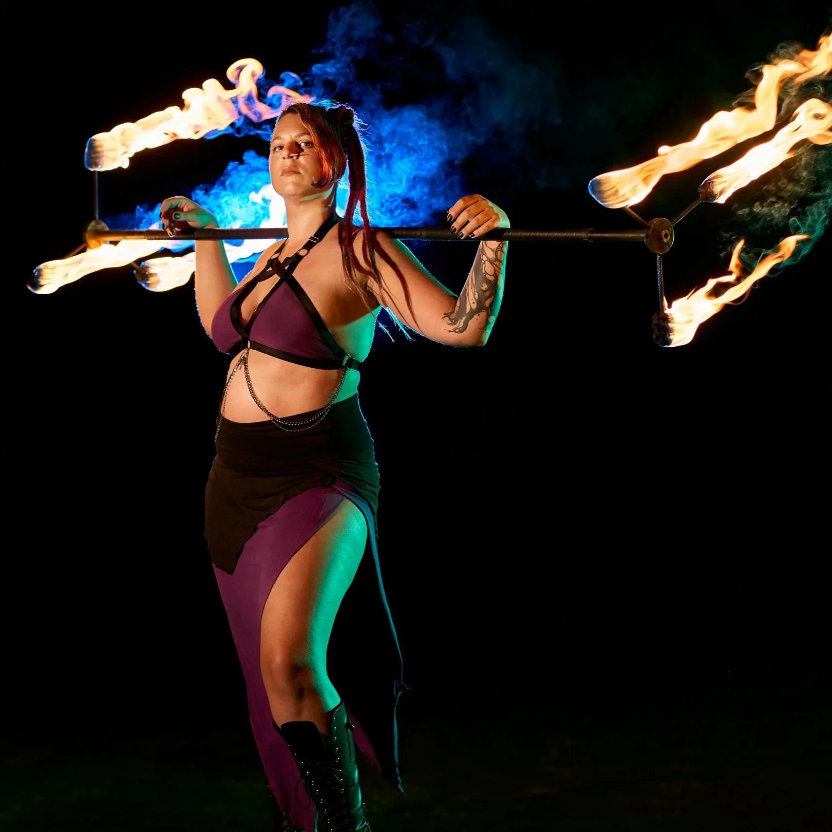 A woman performing fire spinning with a fire staff against a dark background, with flames emitting from both ends of the staff.