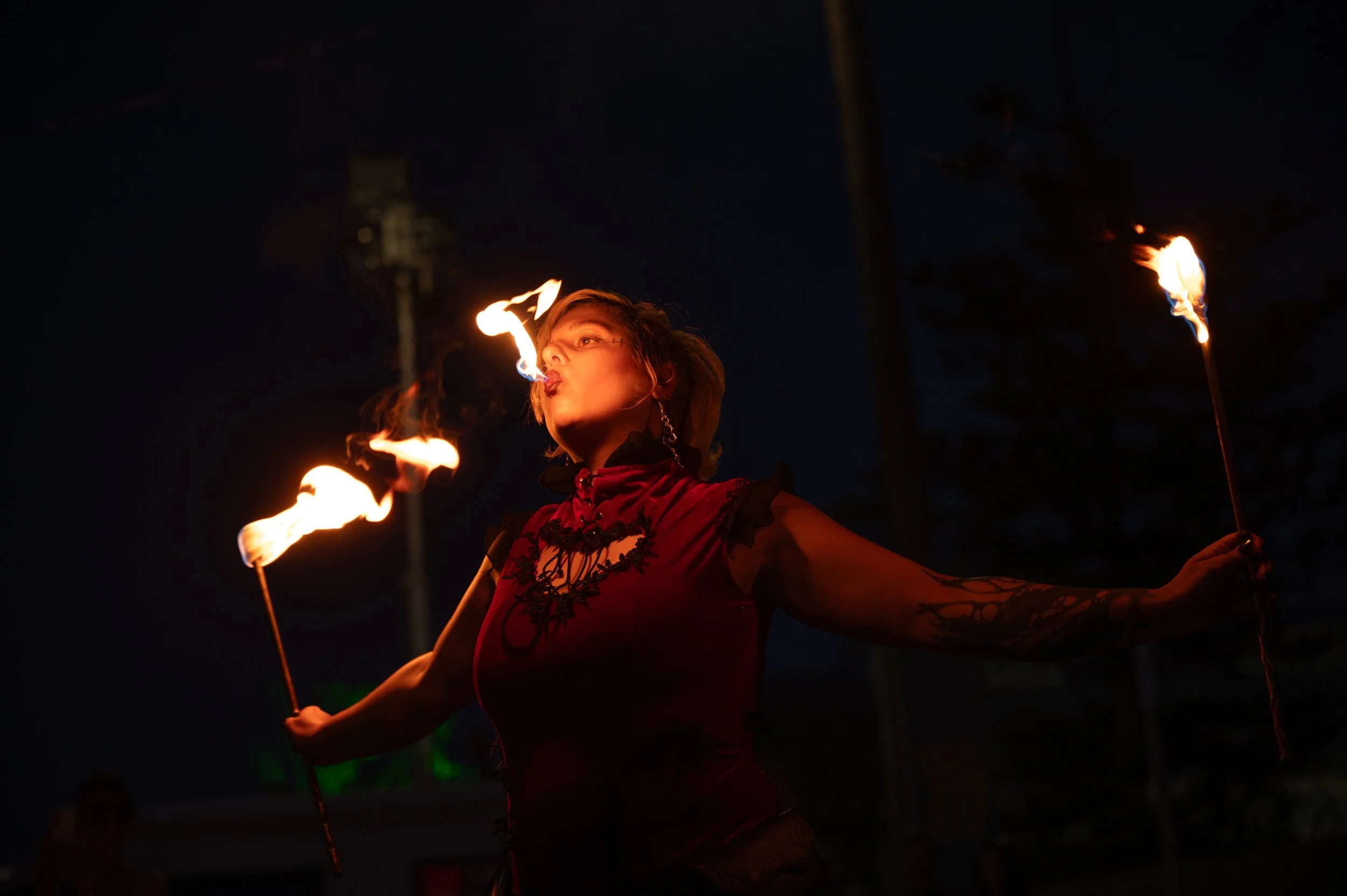 A woman performing fire dancing at night with flames in her hands, wearing a red dress and earrings.
