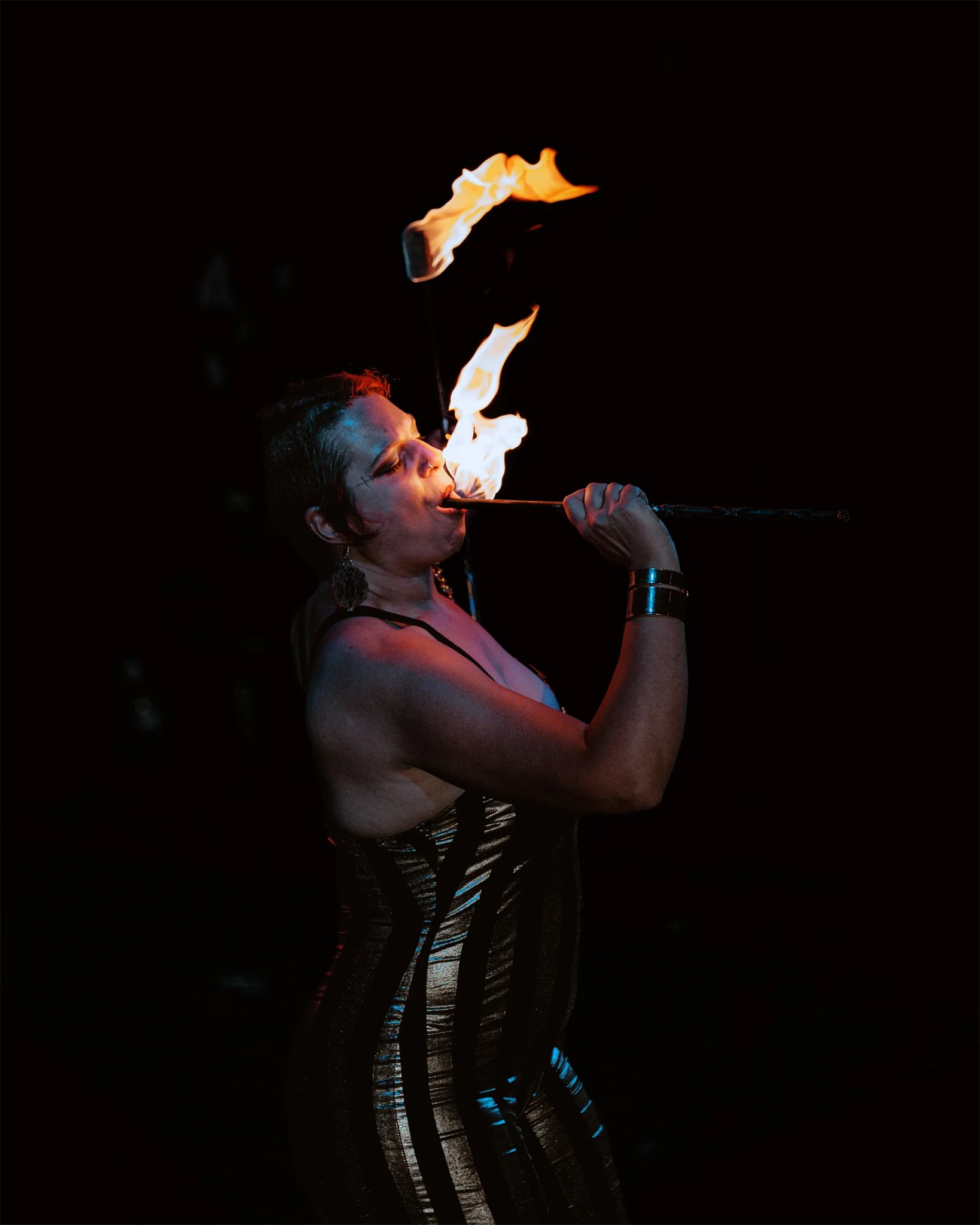 Performer in striped attire performing fire breathing at night.