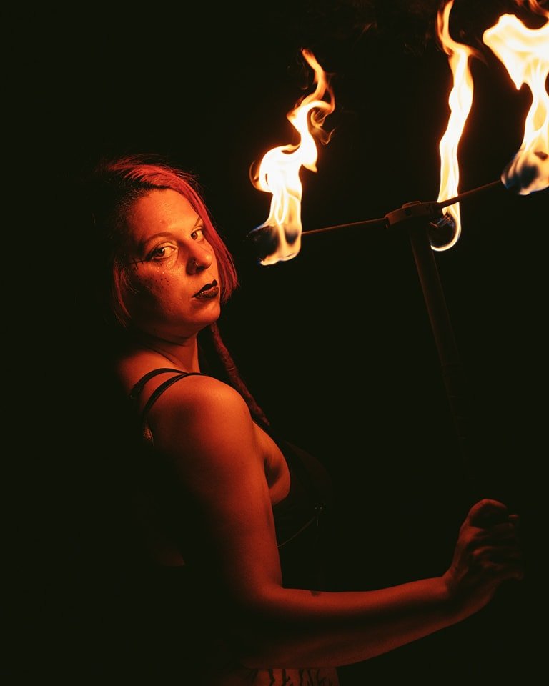 A woman with red hair and dark clothing performing fire spinning in the dark.
