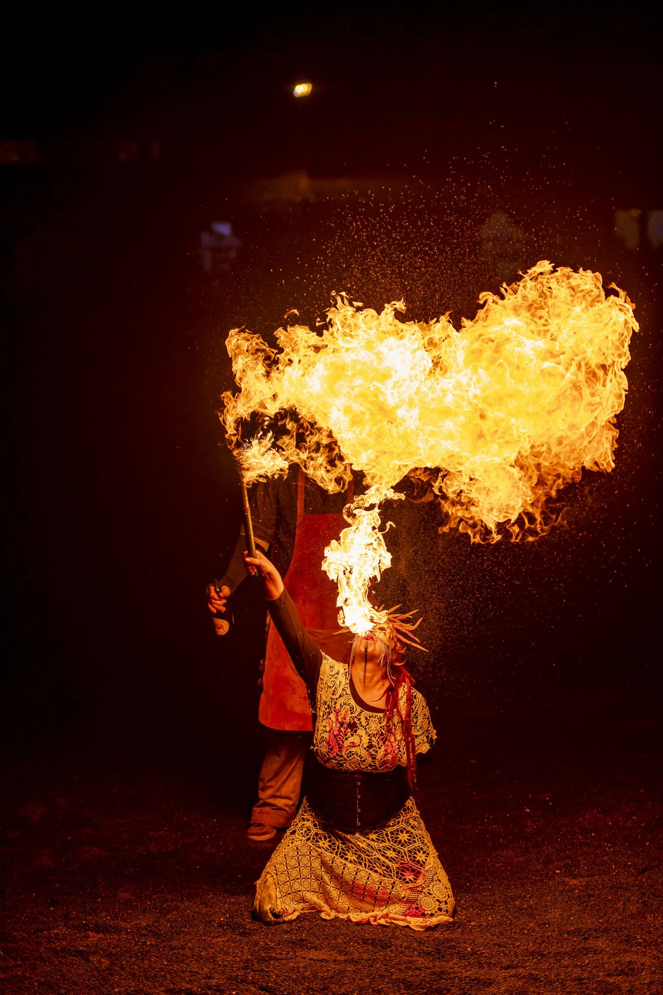 A woman performing fire breathing at night, expelling a large flame projected into the shape of a heart.