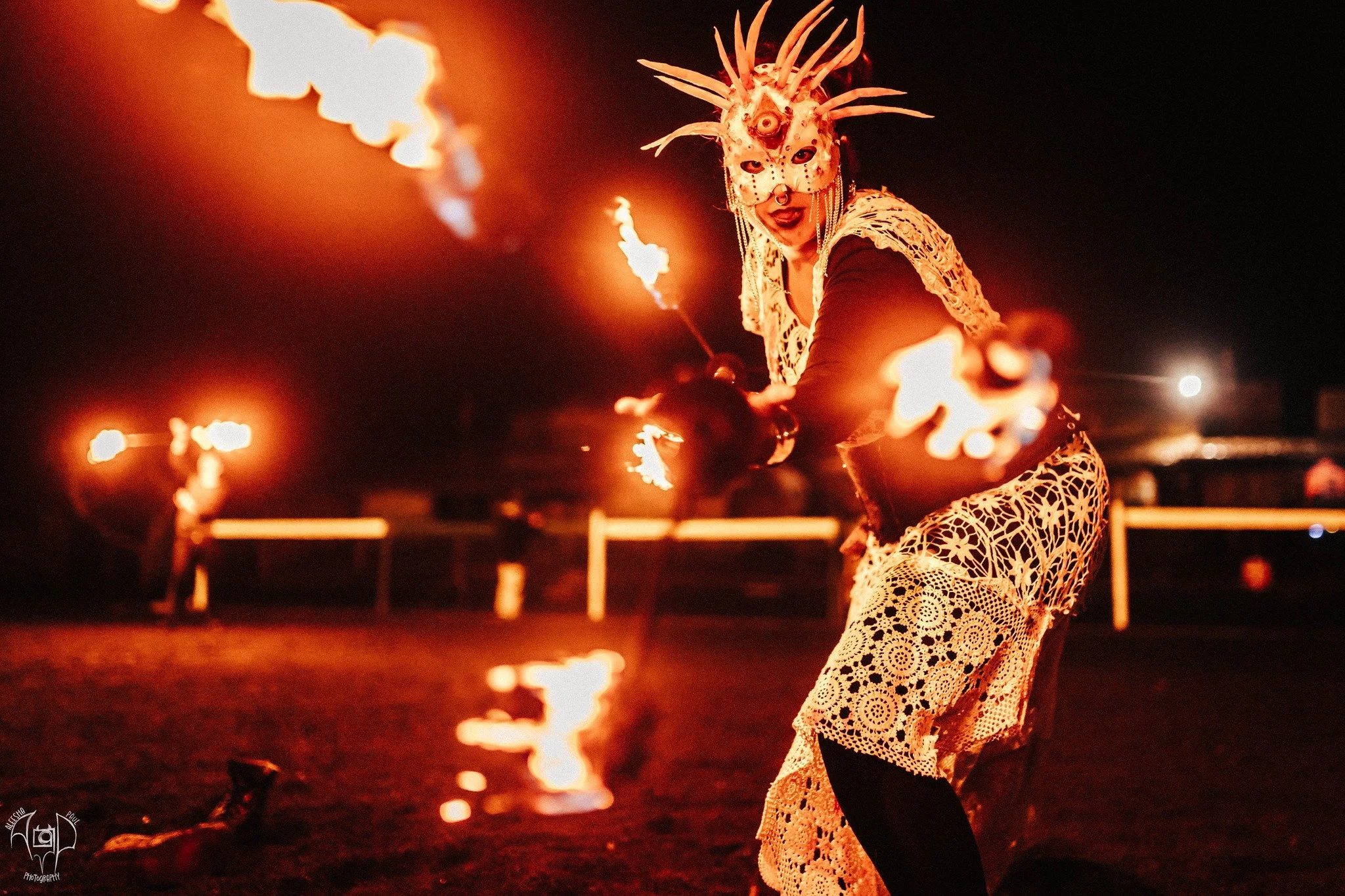 Person in an elaborate hay-themed costume performing fire juggling at night.