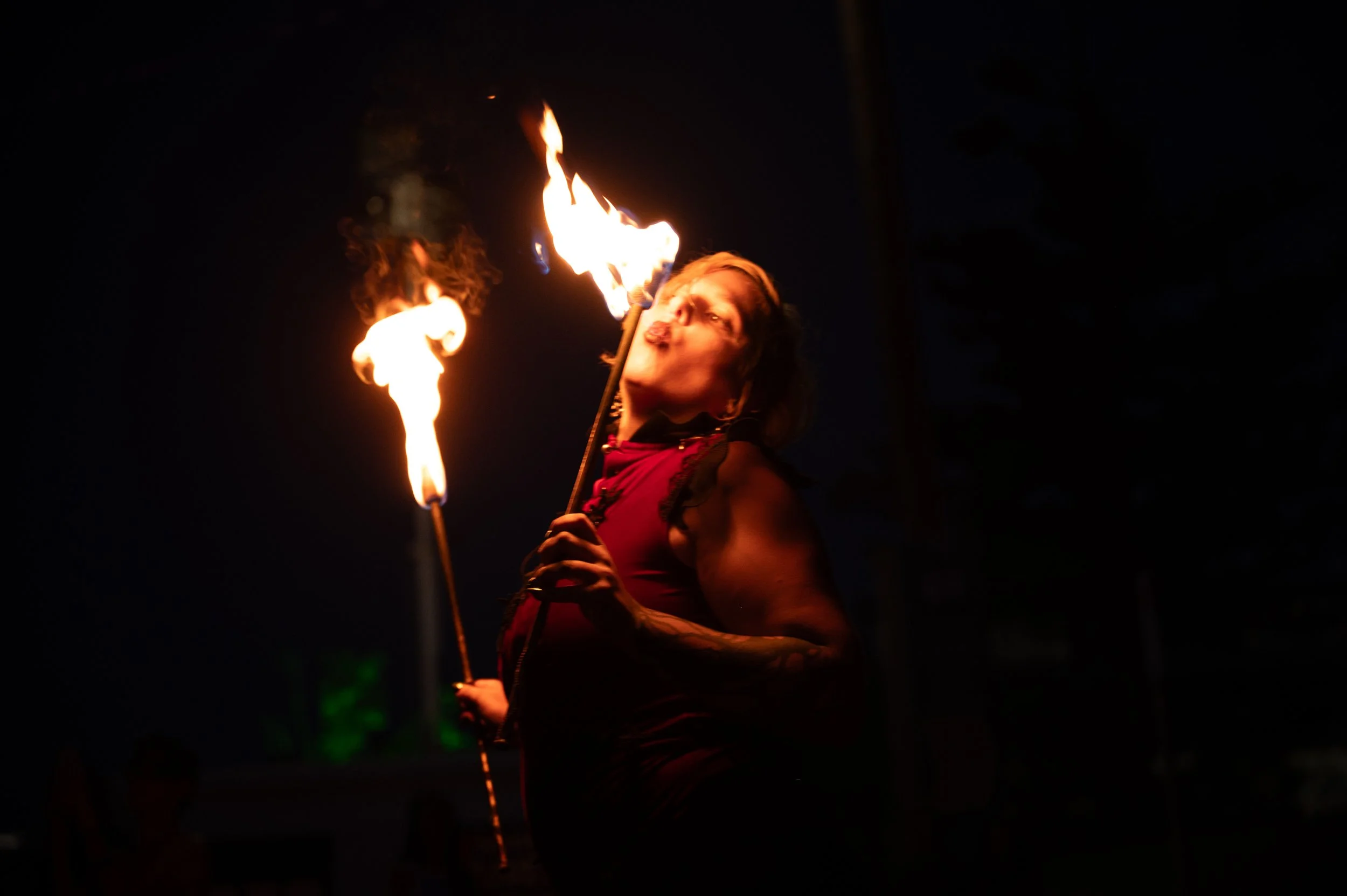 A woman performing a fire-eating act at night, with flames emerging from her mouth and torch.