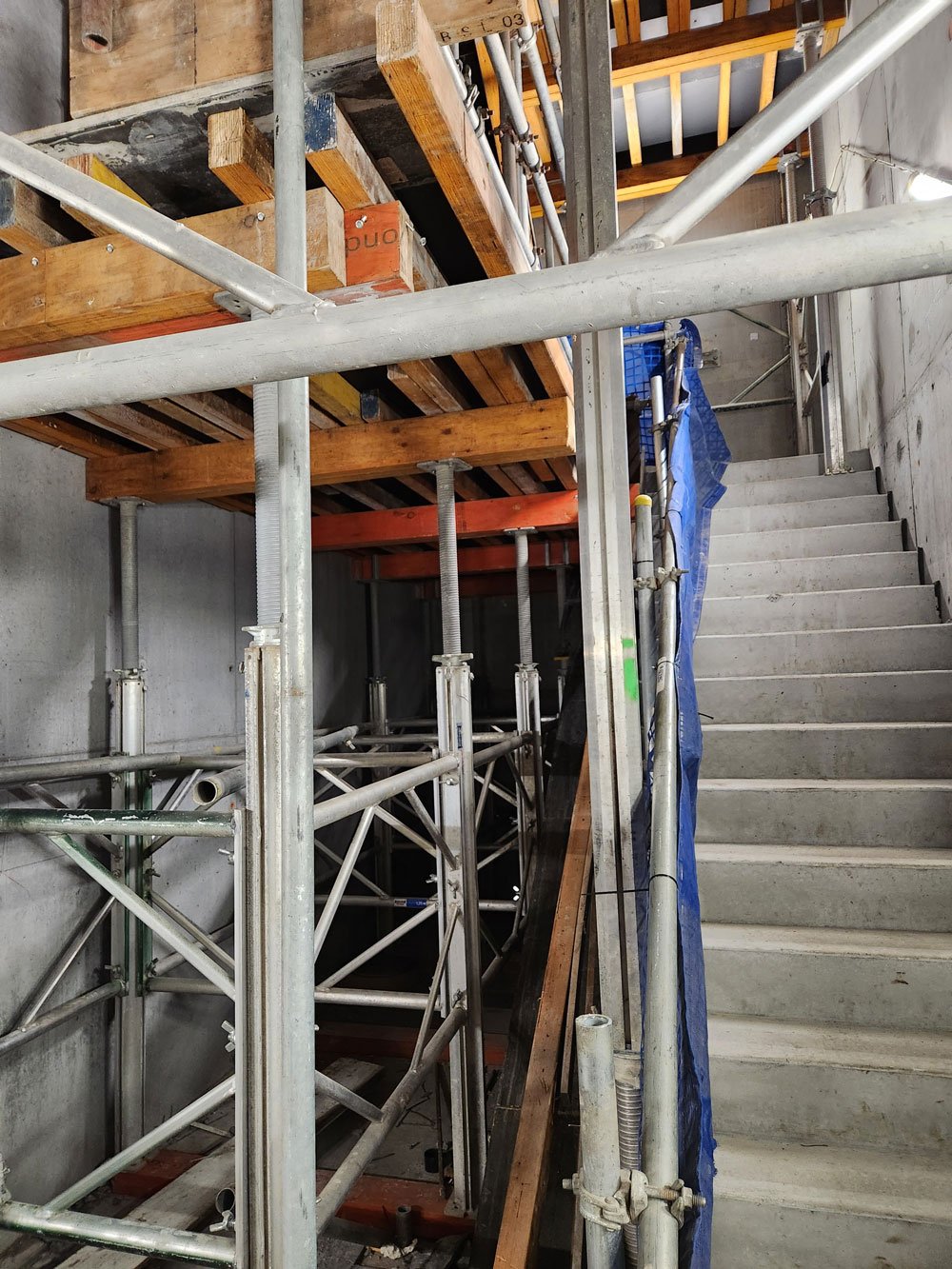 Construction site with metal scaffolding, wooden floor structures, and concrete stairs.