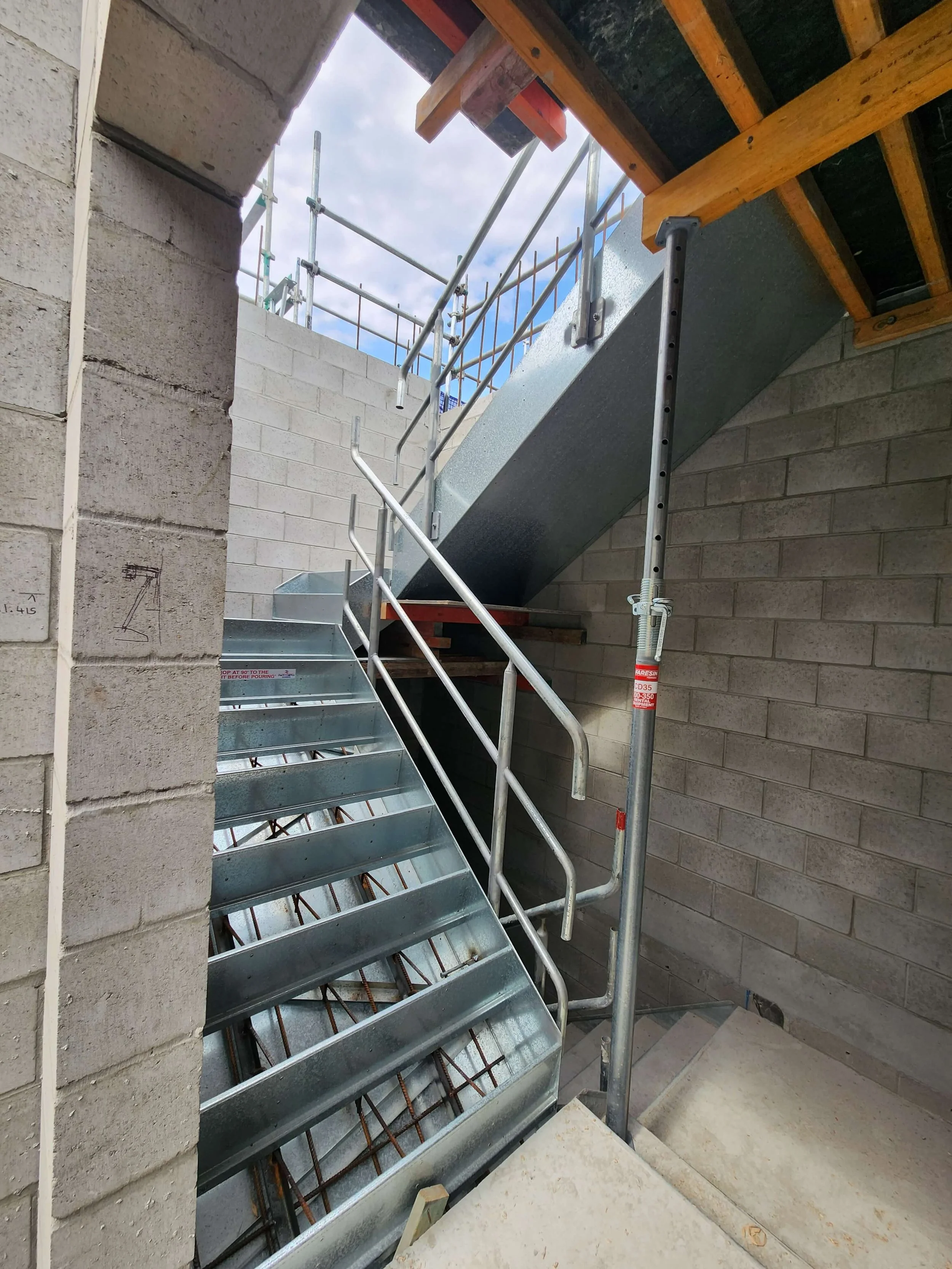 Construction site with metal staircase and safety railing, unfinished walls, and scaffolding outside
