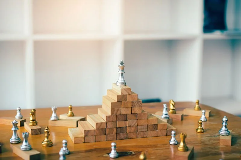 Chess set with a pyramid of wooden blocks and a silver king chess piece at the top on a wooden table.