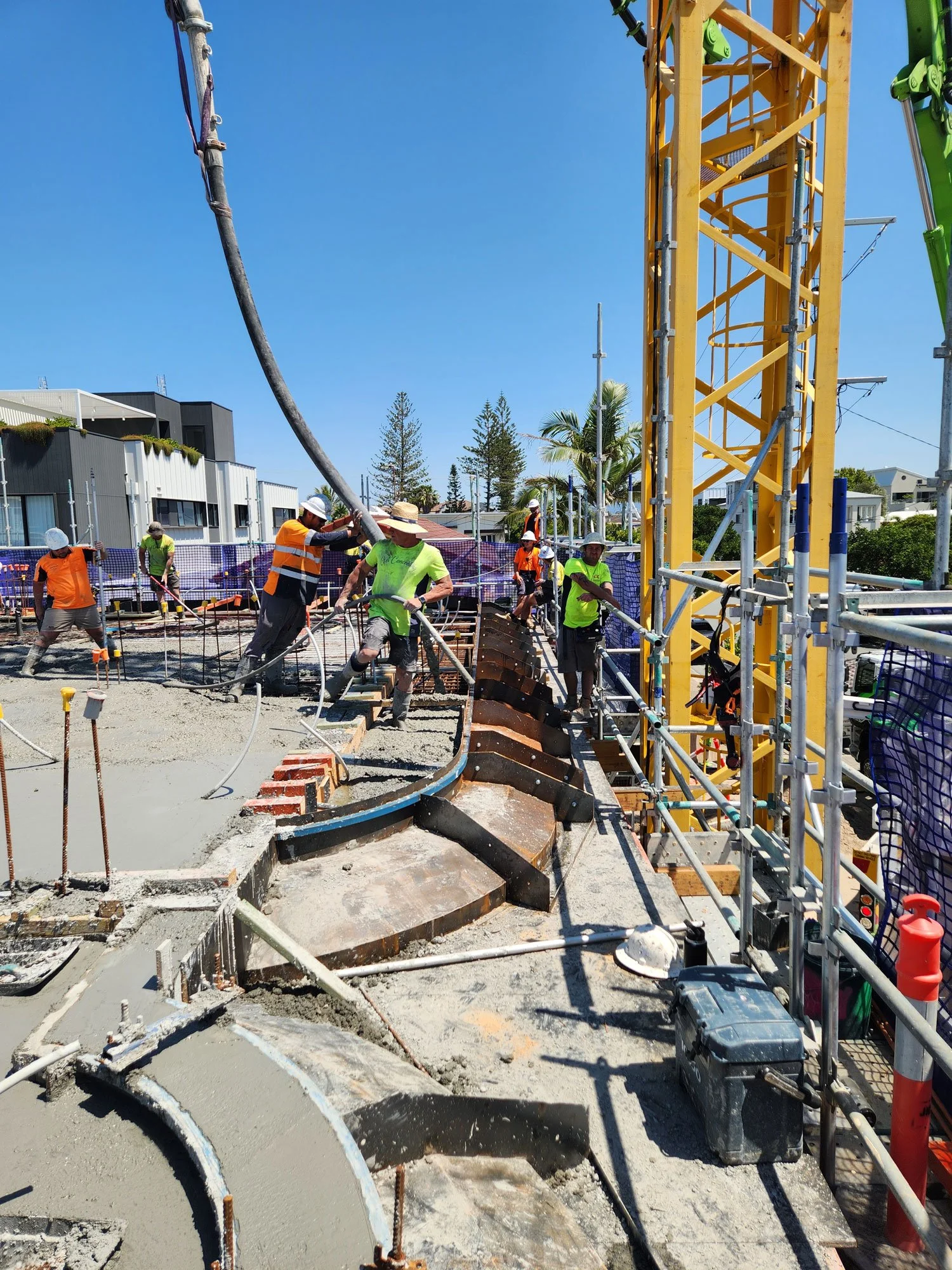 Construction workers pouring and leveling concrete on a building site with a large yellow crane and safety gear.