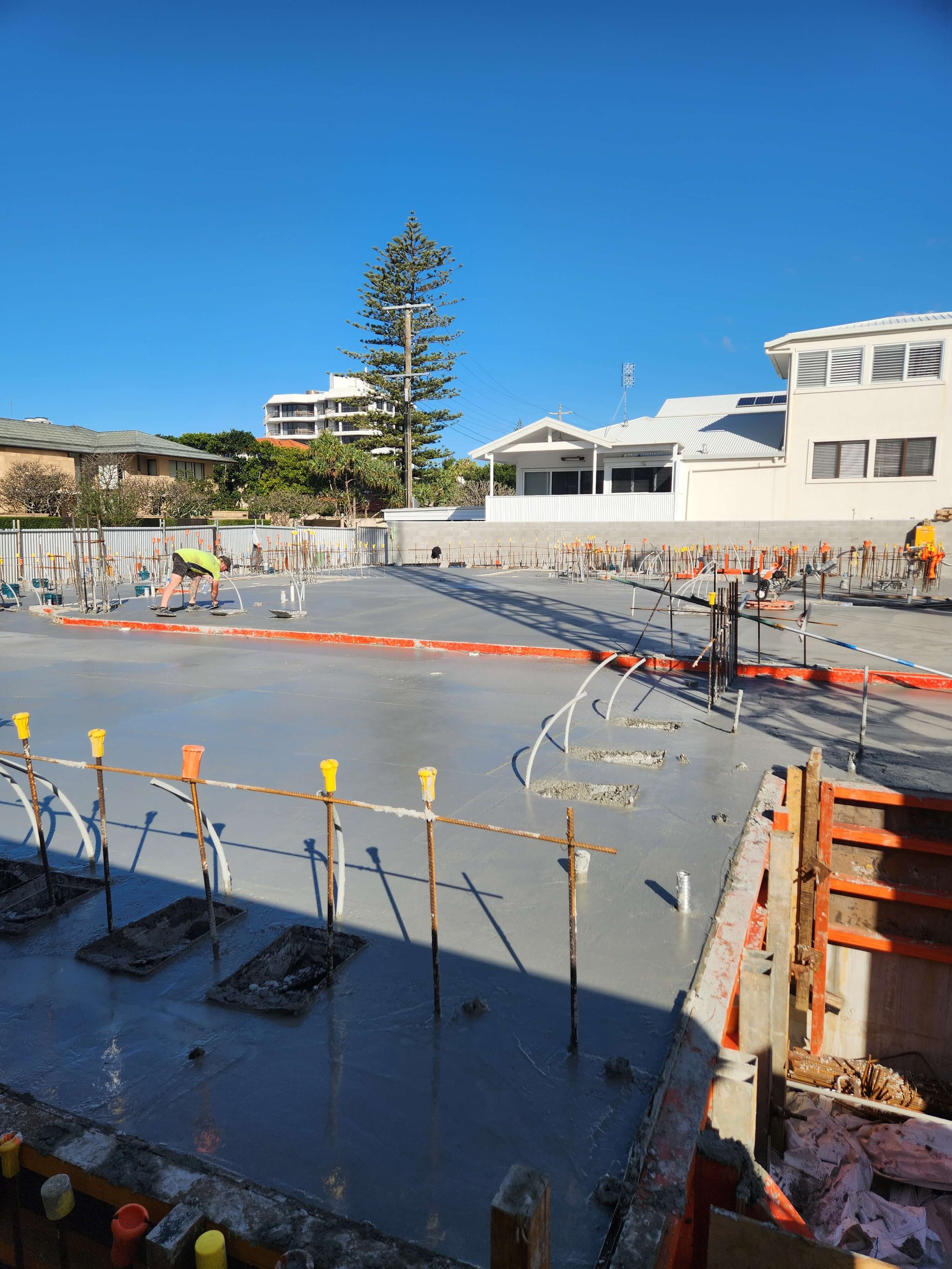 Construction site with workers pouring a concrete slab for a building foundation on a bright, sunny day.