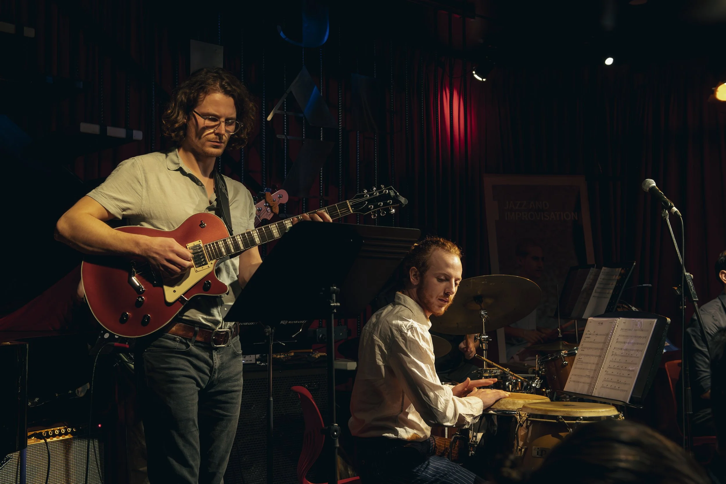 A Melbourne jazz band performing on stage with a guitarist, a pianist, and another musician, with red and dark stage lighting.