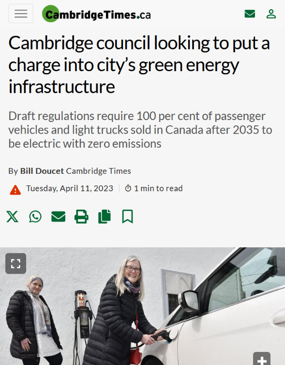 Two women charging a white electric car at an outdoor charging station against a white wall.