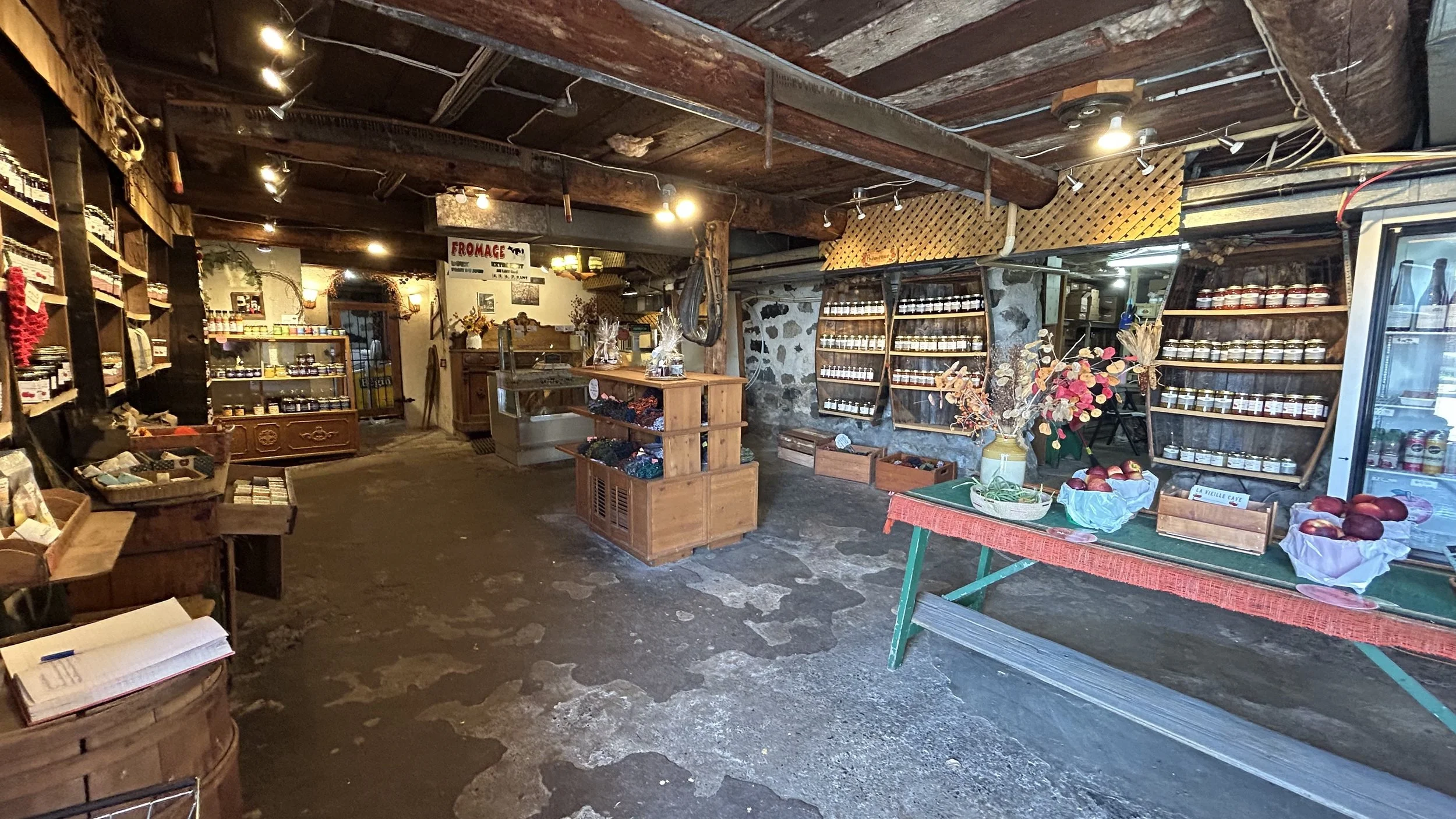 Magasin d'épicerie ou marché intérieur avec étagères de bocaux, un présentoir de pommes, et un comptoir en bois, ambiance rustique avec poutres en bois.