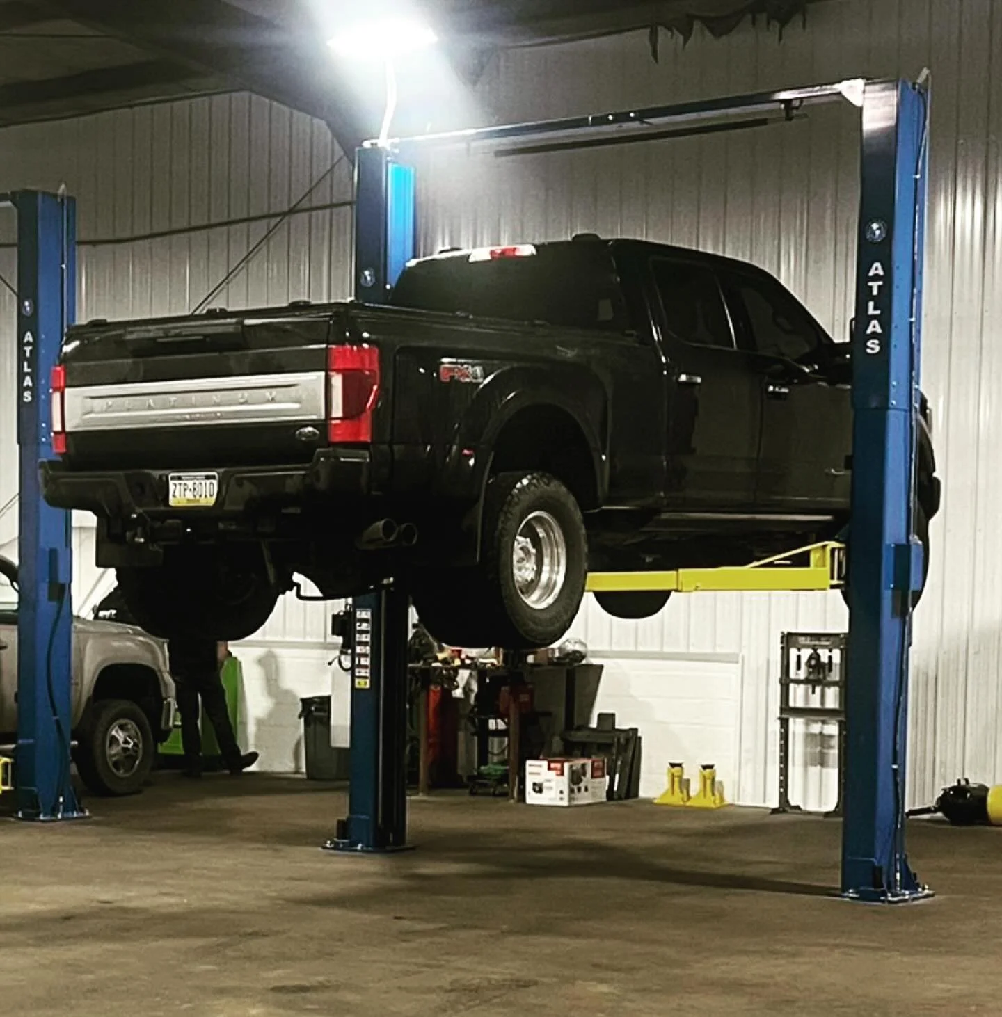 A black pickup truck is lifted on a blue hydraulic car lift inside a garage or repair shop.