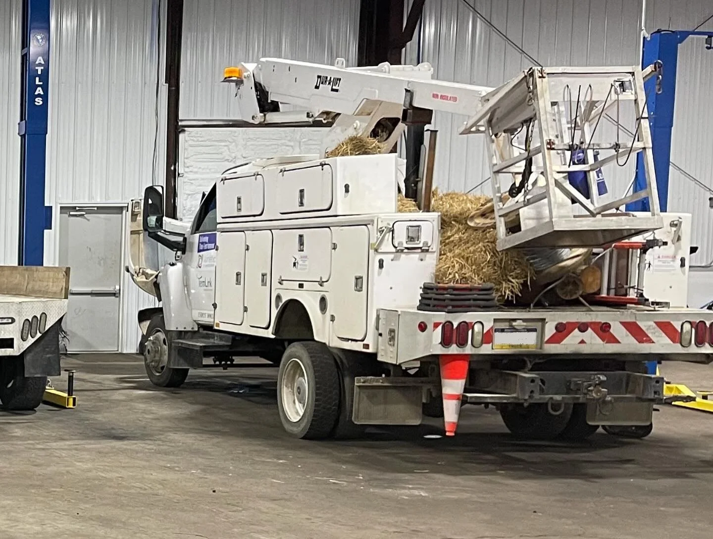 A utility truck with an elevated bucket and storage compartments parked inside a warehouse, surrounded by equipment and a concrete floor.