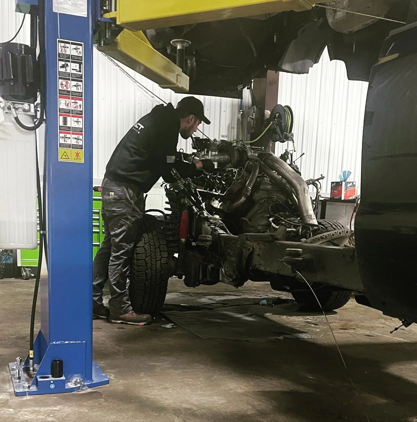 A mechanic working on the engine of a vehicle that is mounted on an automotive lift in a garage or workshop.