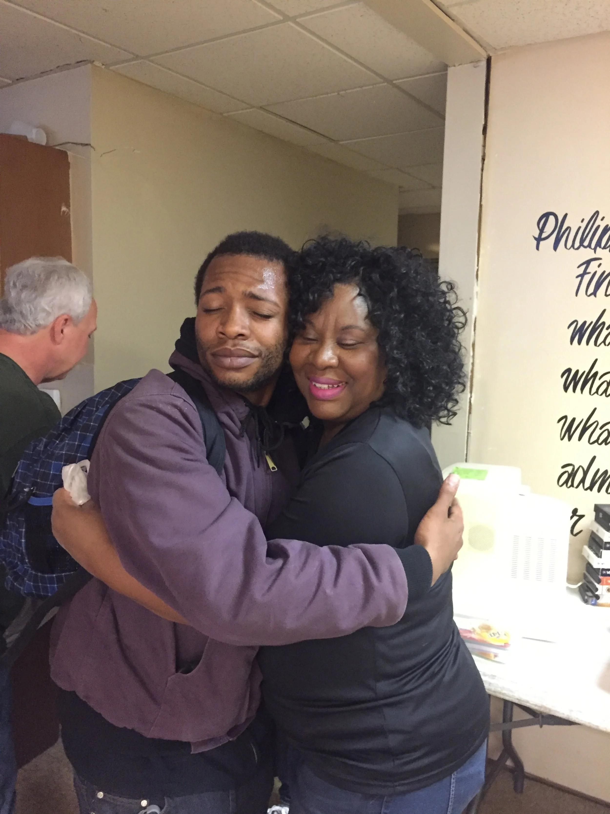 Two people hugging and smiling at each other in an indoor setting.