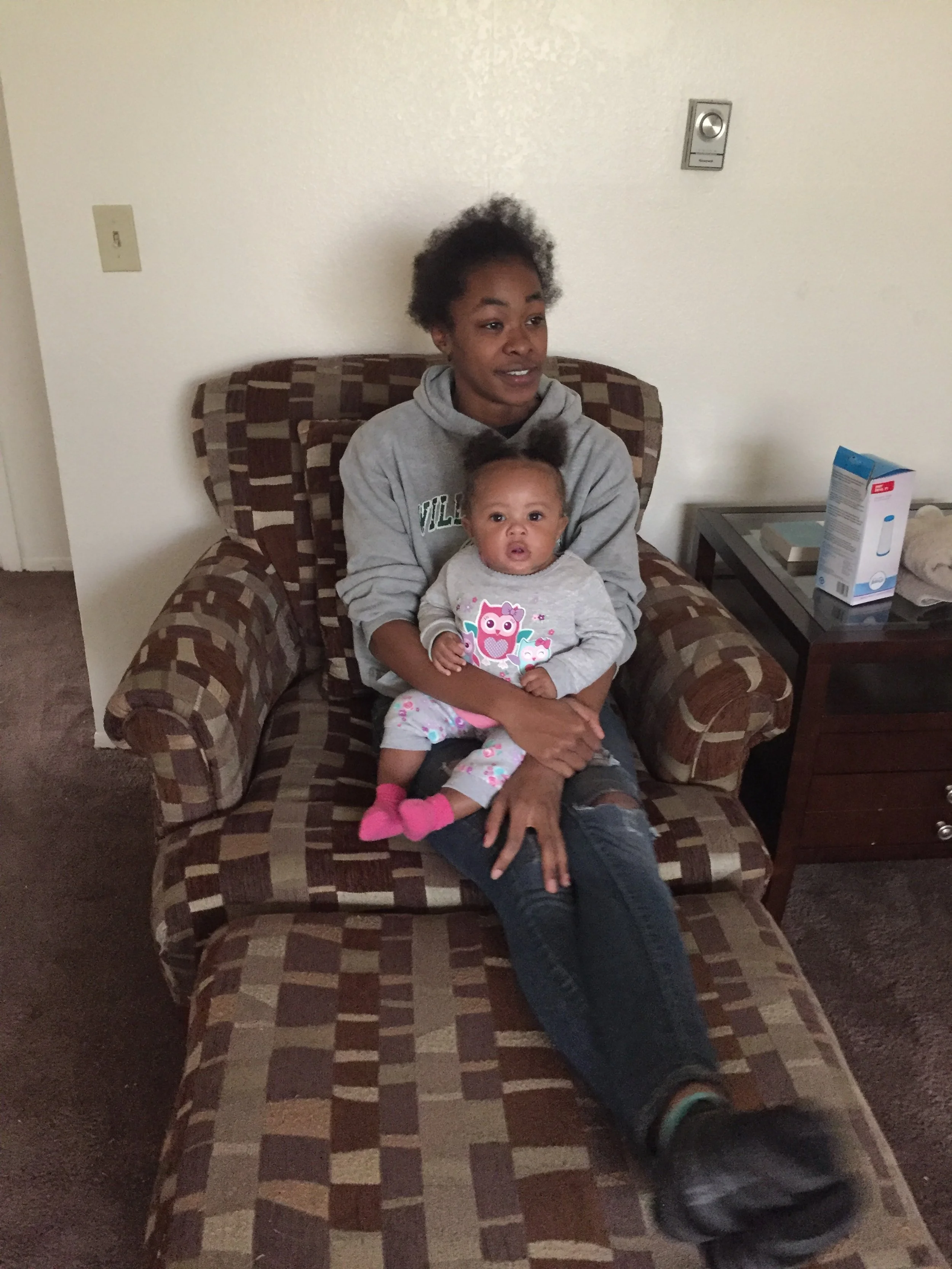 A woman sitting on a patterned couch with a young girl on her lap in a living room.